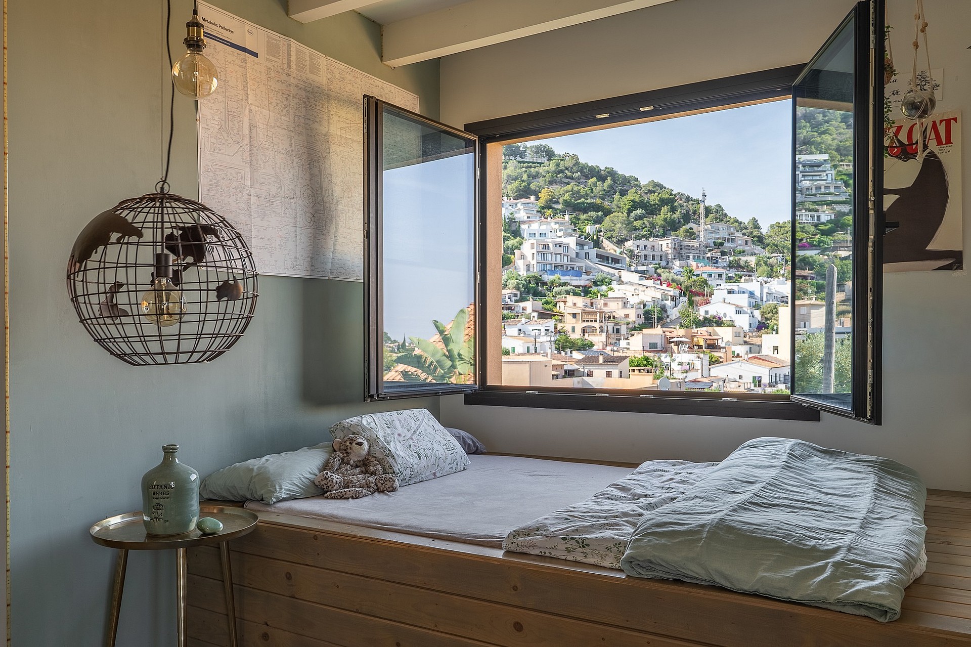 Interior bedroom view featuring an open casement window overlooking a hillside town in Genova with mountain slopes visible.