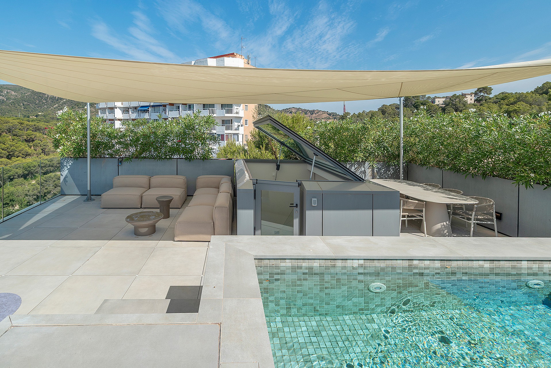 Rooftop terrace featuring a tiled swimming pool, modular beige sofa, dining area, and a beige shade canopy under clear skies.