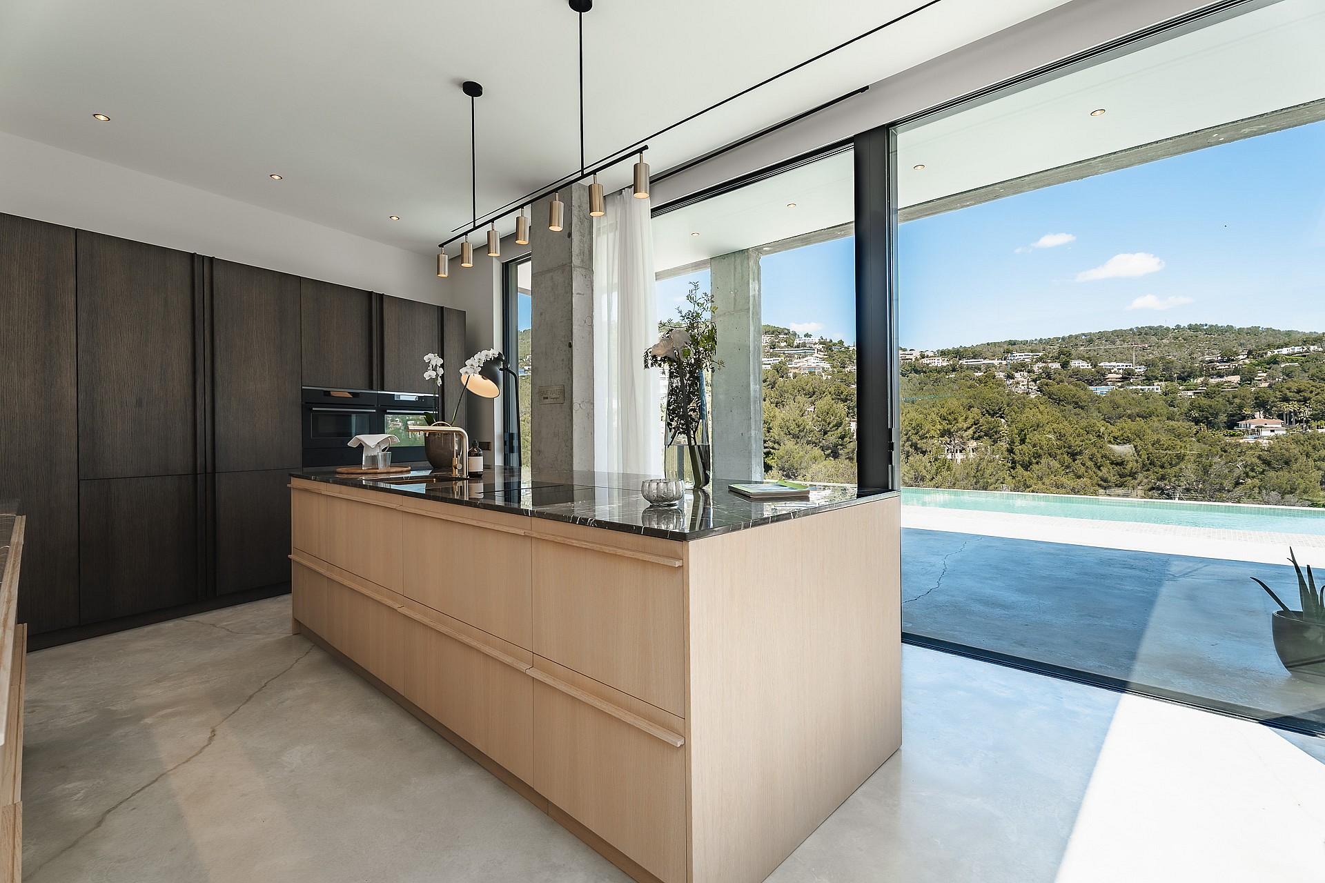Contemporary kitchen featuring a light oak island, dark wood cabinetry, and large glass doors opening to a pool terrace.