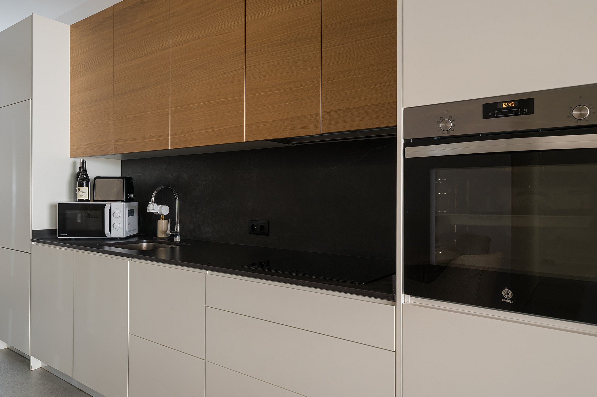 Modern kitchen featuring matte beige lower cabinets, wood veneer upper cabinets, and a black stone countertop.
