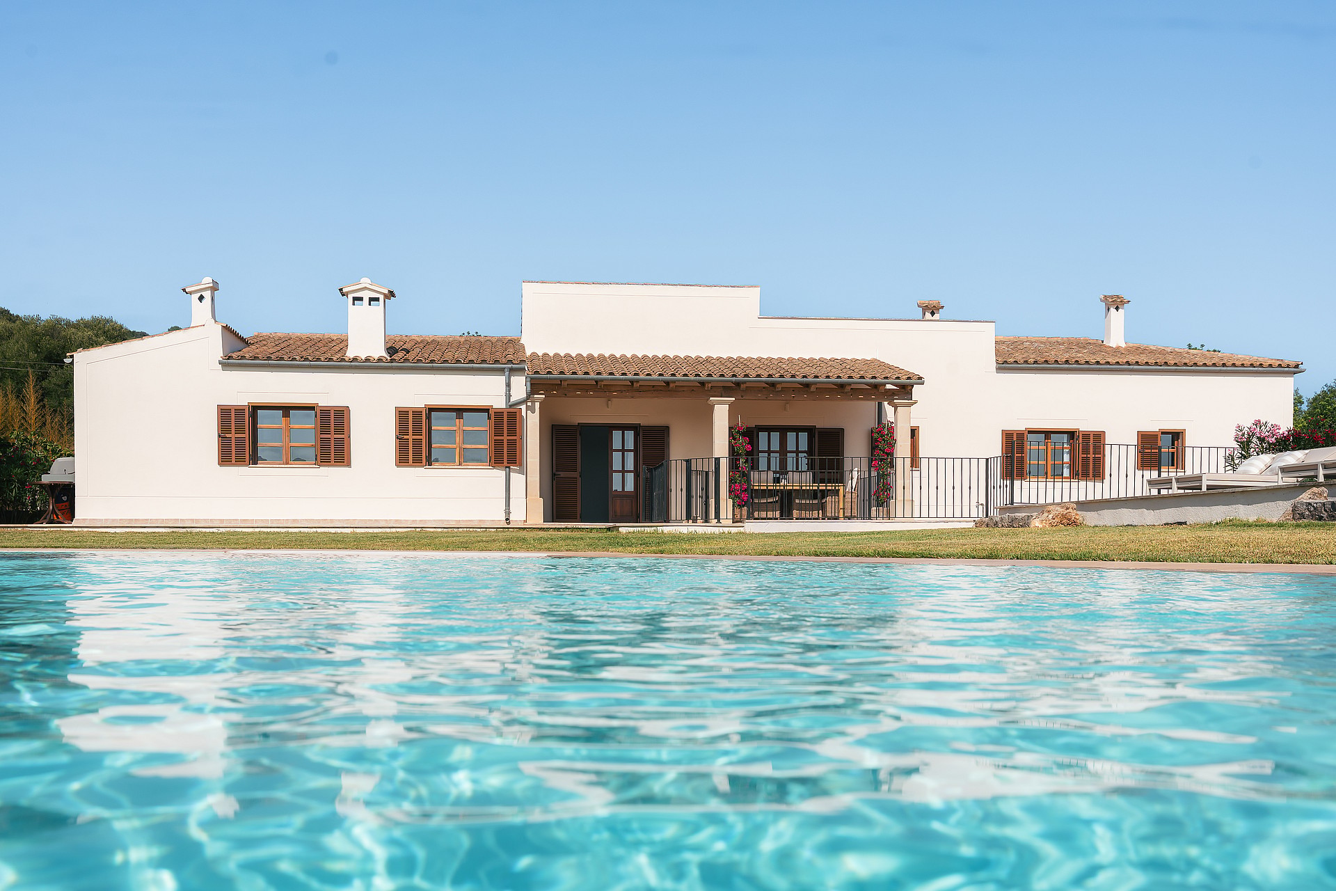 Vista de una finca blanca de una planta con tejado de teja árabe junto a una piscina azul bajo el cielo despejado.