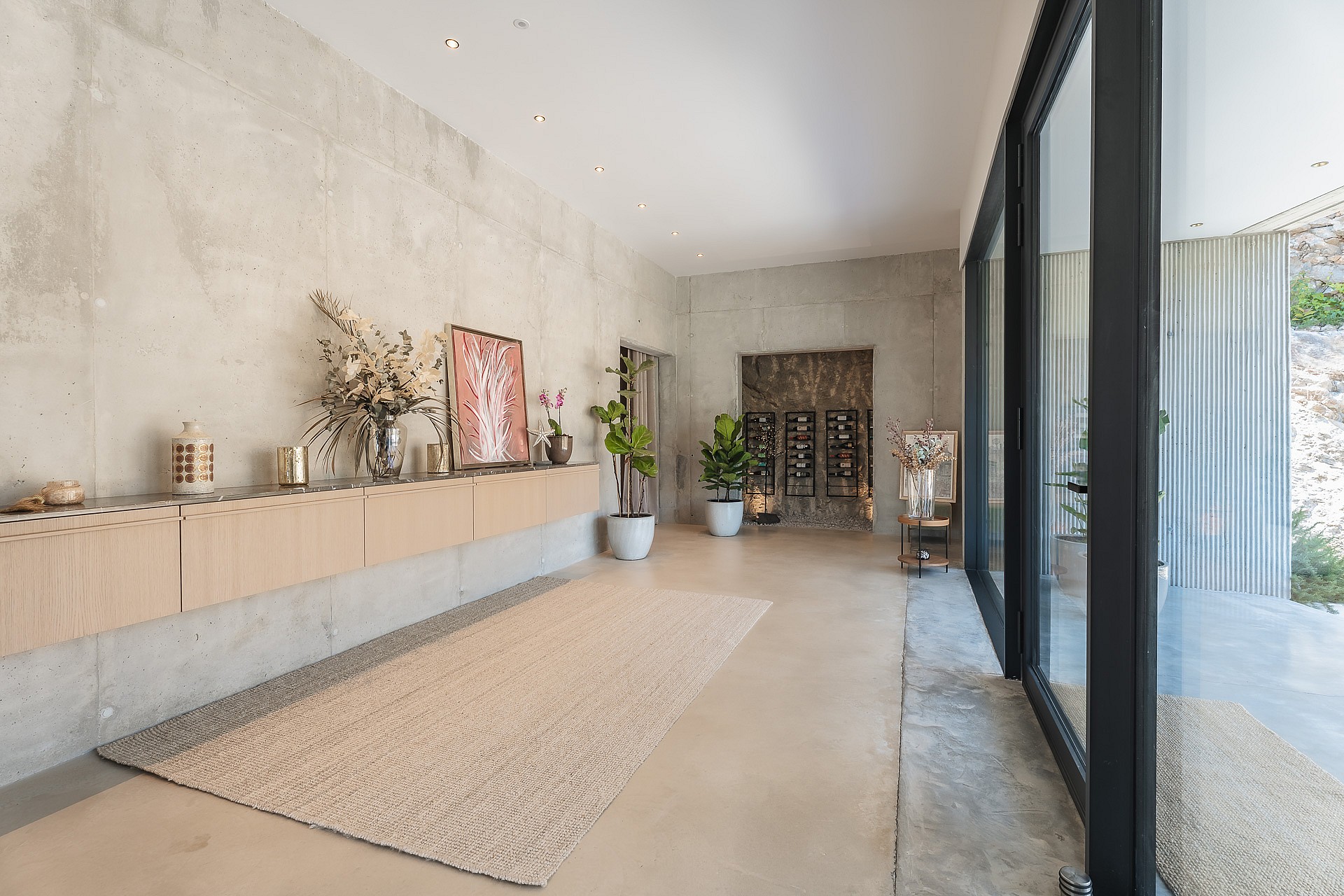 Minimalist hallway featuring raw concrete walls, floating oak storage, and a professional wine display at the far end.
