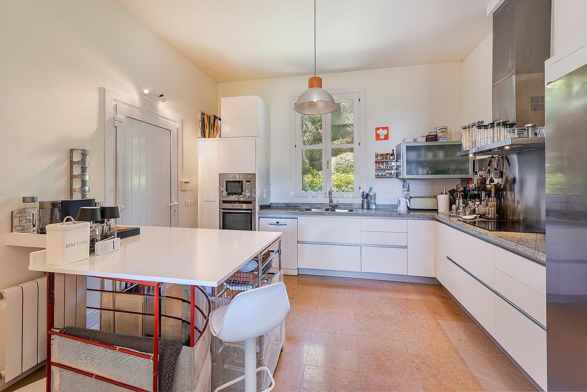 Contemporary white kitchen with stainless-steel appliances, island workstation, and glass doors opening to terrace