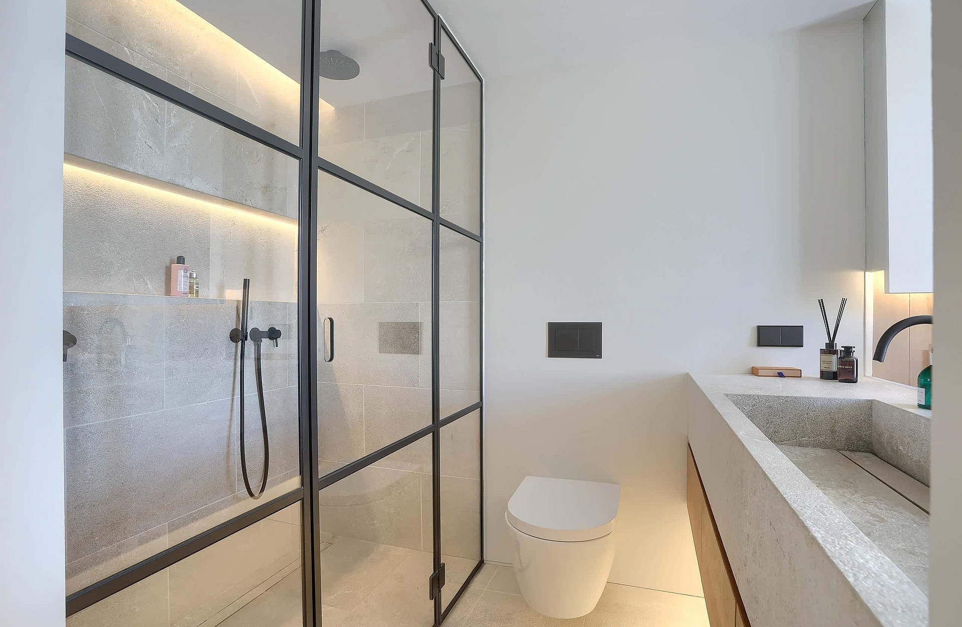 A bathroom featuring a walk-in shower with a black metal-framed glass partition, a stone-composite sink, and minimalist white walls.