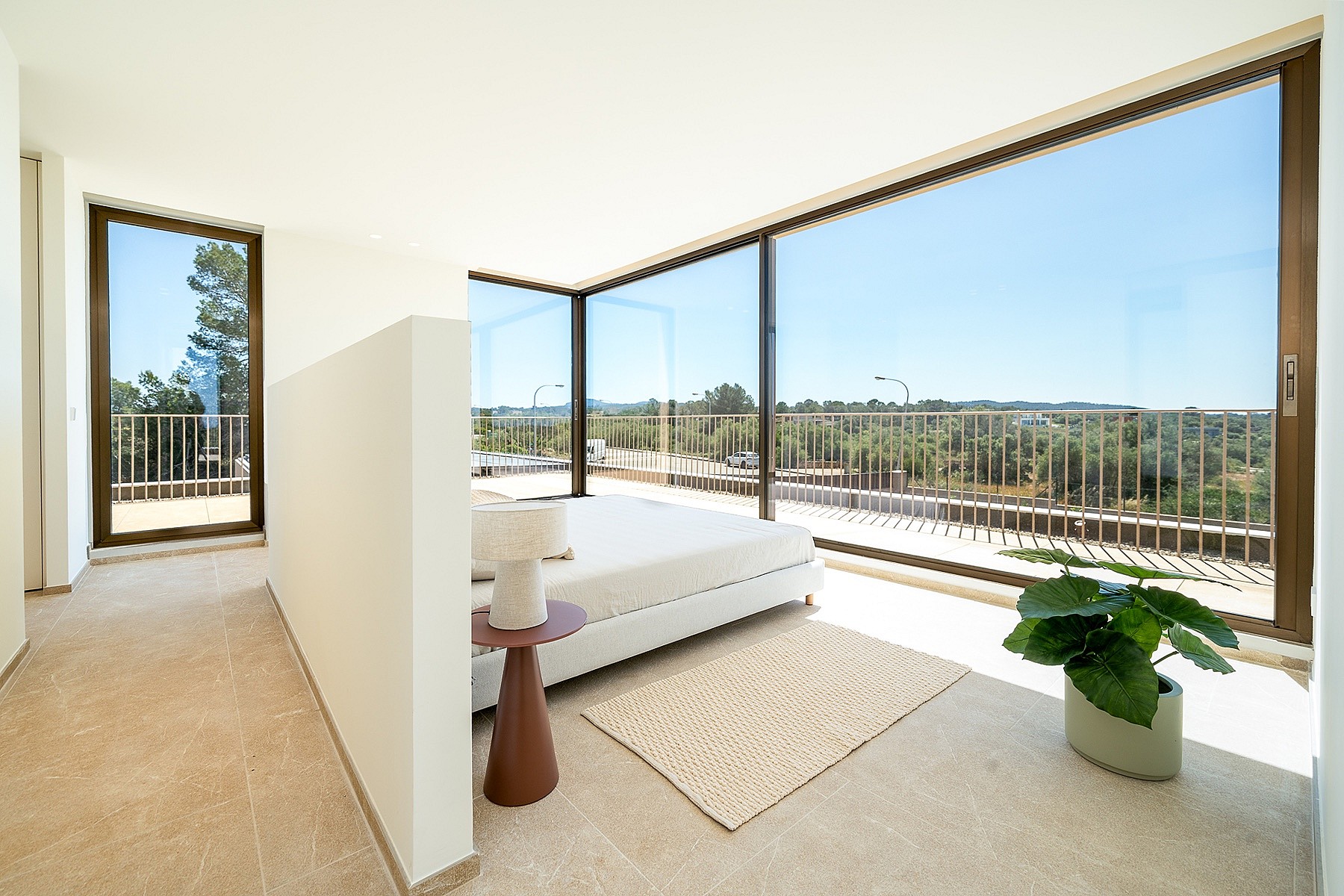 A modern master bedroom with minimalist decor, white bed, stone flooring, and expansive glass walls looking out over green hills.