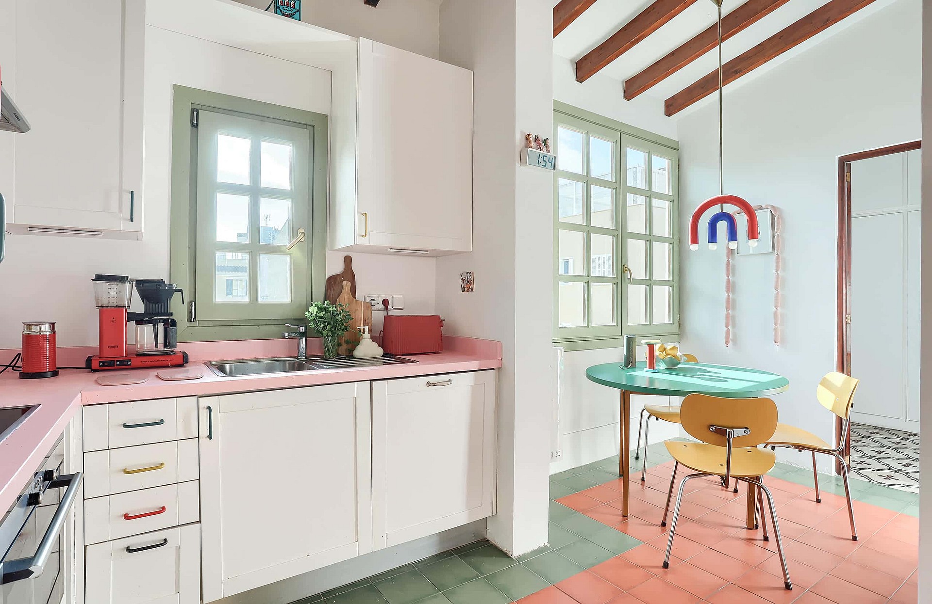 Kitchen featuring white cabinetry, a pink countertop, and a dining area with a round green table and wood chairs.