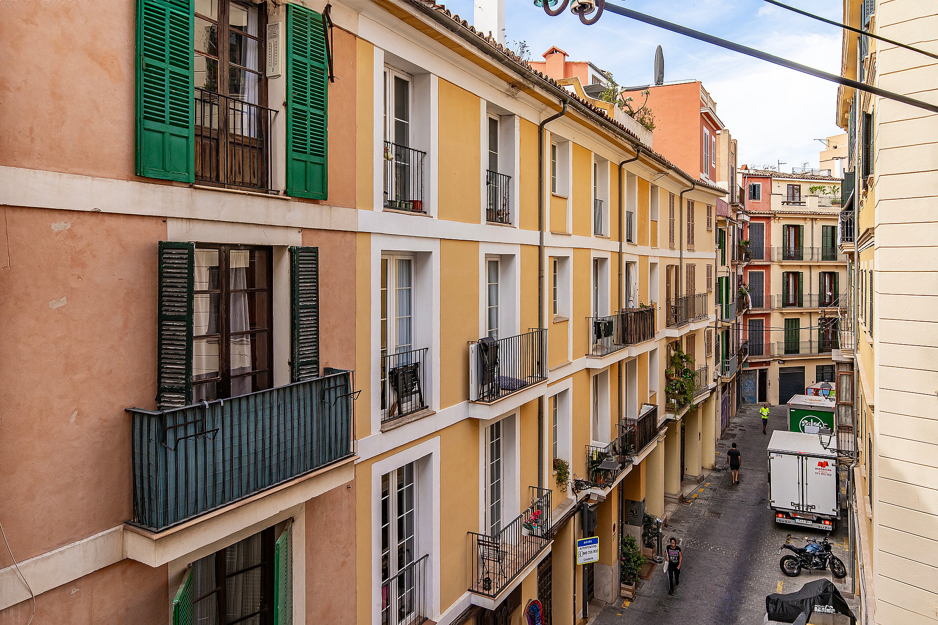 Exterior view of a traditional Mediterranean apartment building facade with mustard-yellow walls and green wooden shutters.