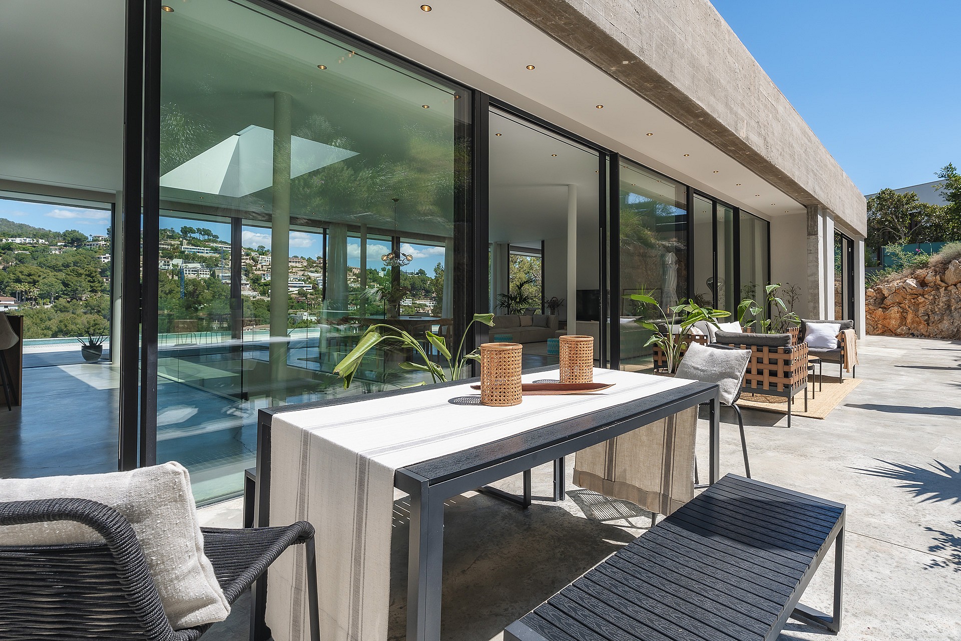 Contemporary stone terrace featuring a black metal dining set and floor-to-ceiling glass doors reflecting mountain views.