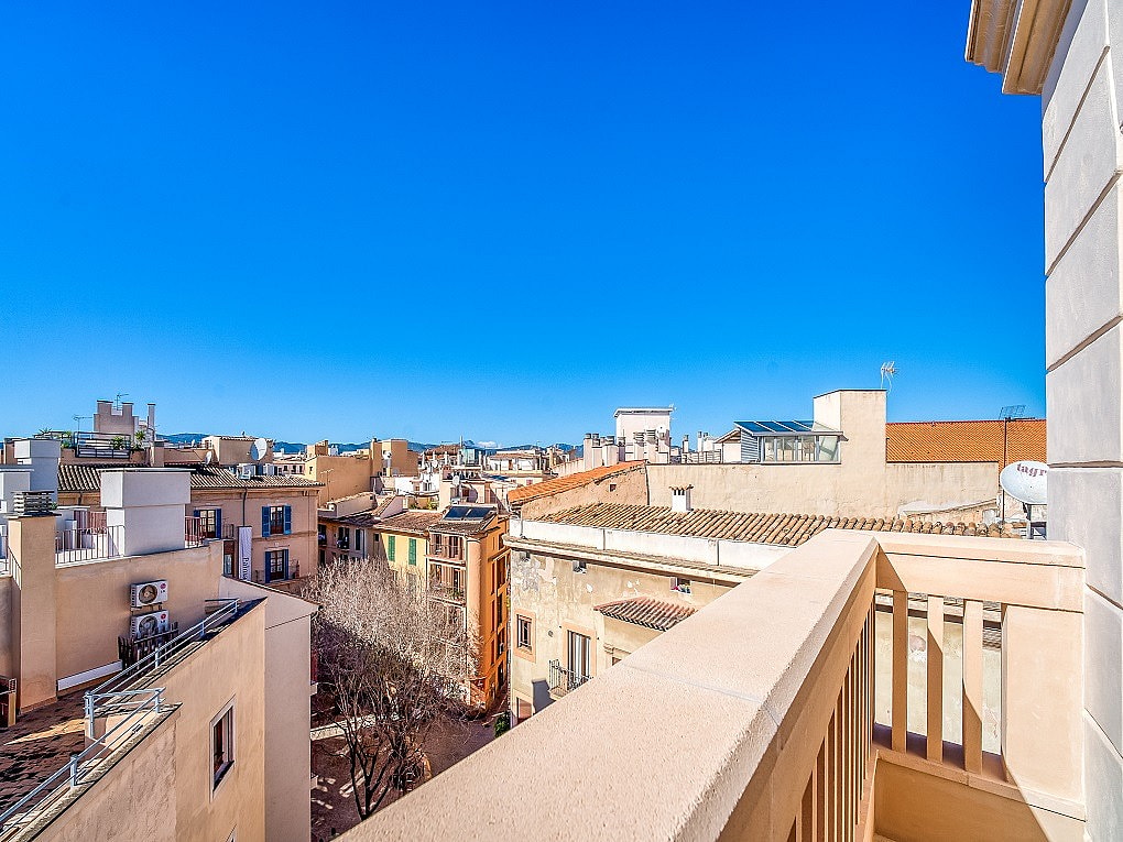 An elevated view from a rooftop terrace looking out over the densely packed stone buildings and terracotta roofs of an Old Town.