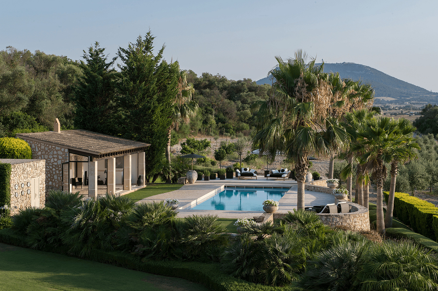 A stone-built finca exterior featuring a rectangular swimming pool, landscaped garden, and mountain views in Algaida.