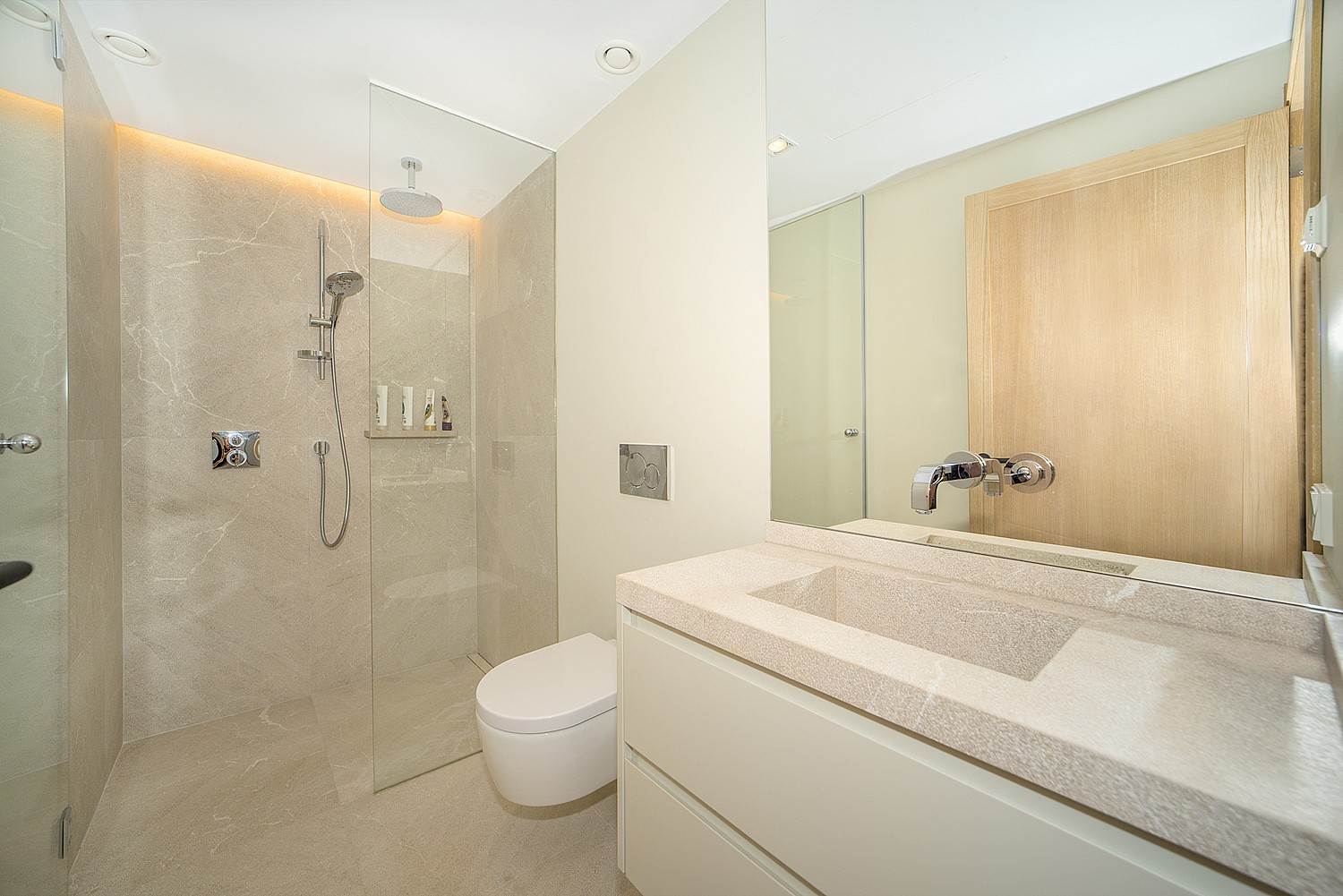 Modern bathroom featuring a beige stone tiled walk-in shower with glass partition, white vanity, and large mirror.