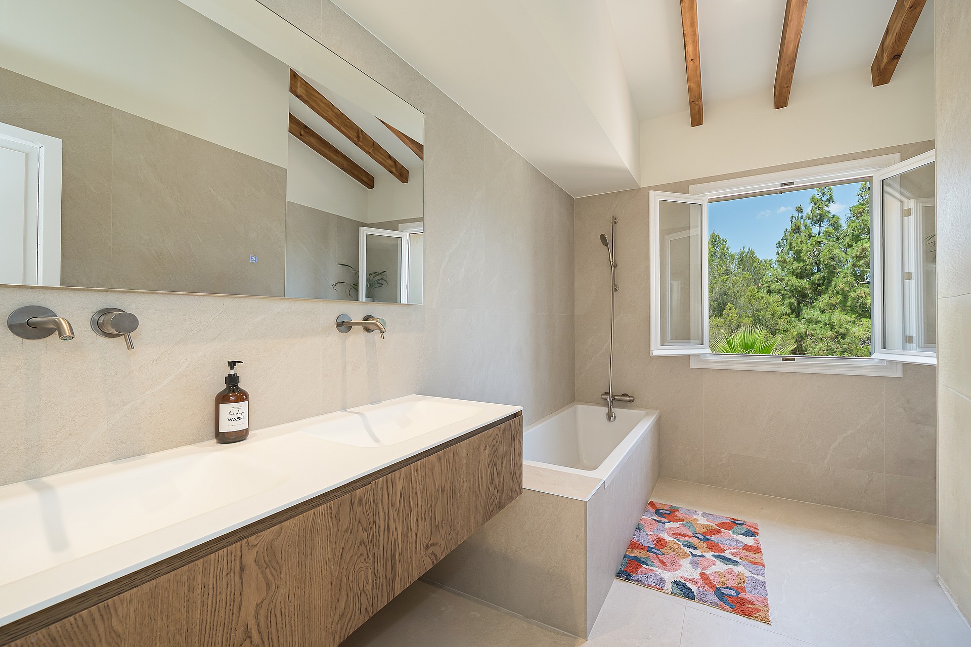 Contemporary bathroom featuring a long oak vanity with double sinks and wall-mounted brushed metal faucets.