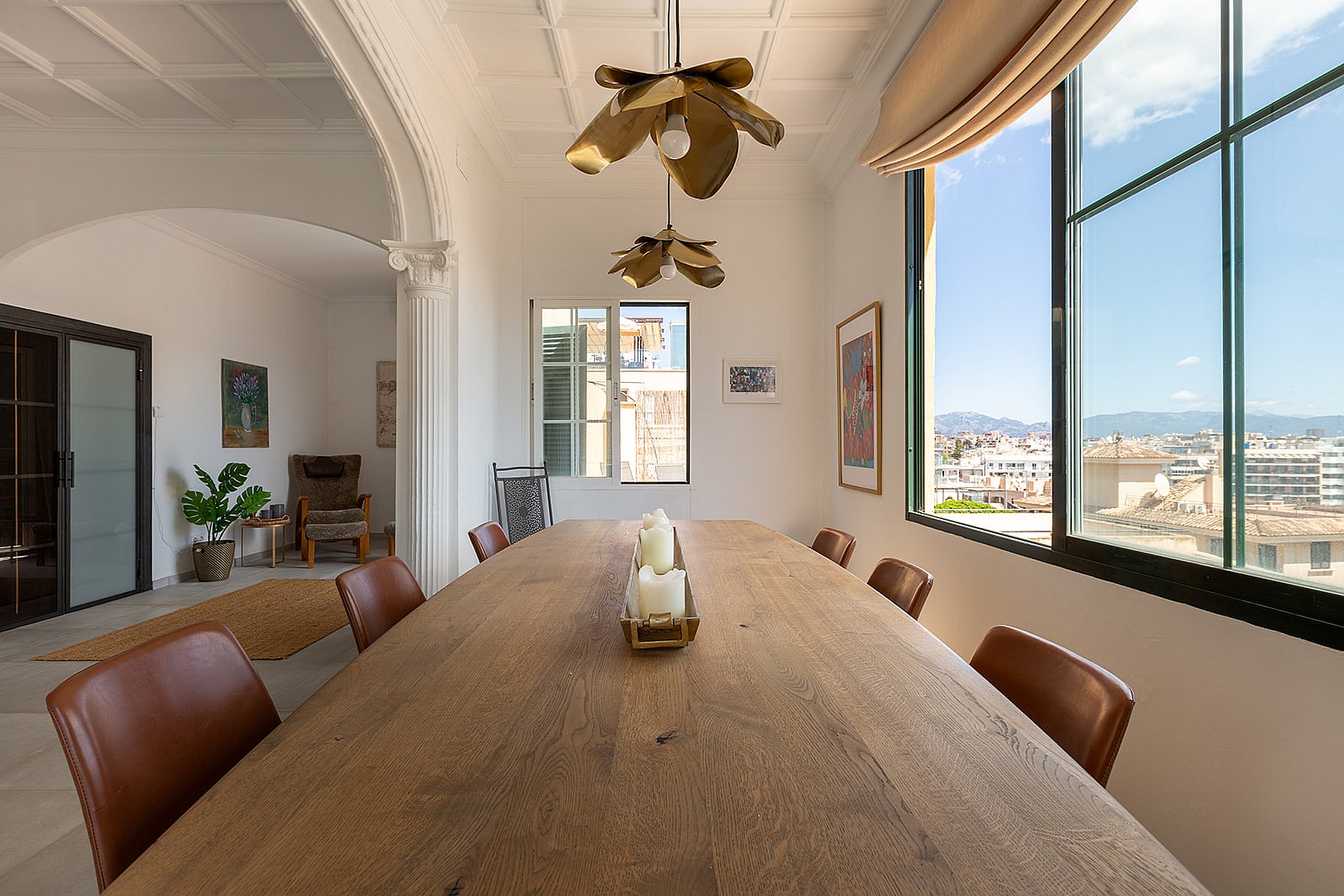 Dining room featuring a long wooden table, leather chairs, and a sculptural gold light fixture beneath a coffered ceiling.