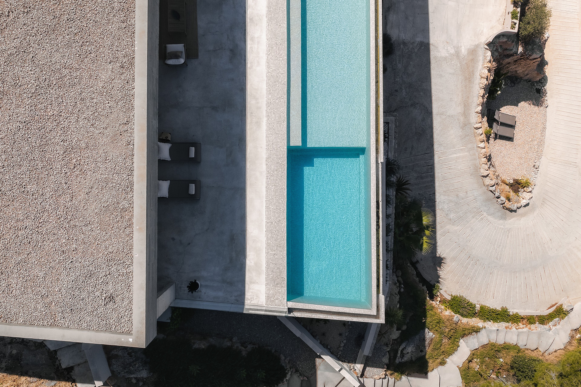 Top-down aerial shot of a rectangular turquoise pool, stone terrace with loungers, and a gravel-topped roof.