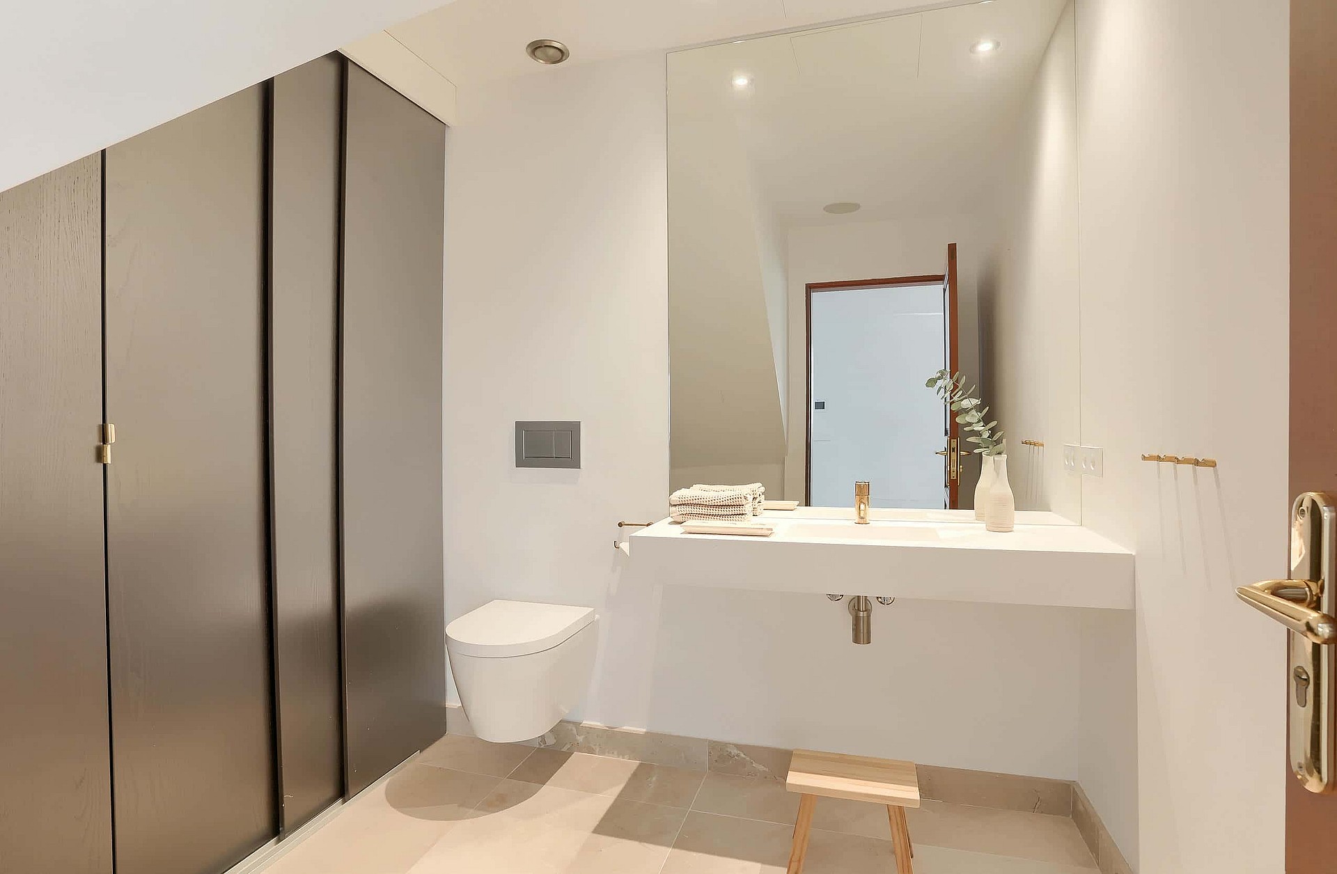 A minimalist bathroom featuring a wall-hung white basin, a wall-mounted toilet, and tall grey floor-to-ceiling cabinetry.