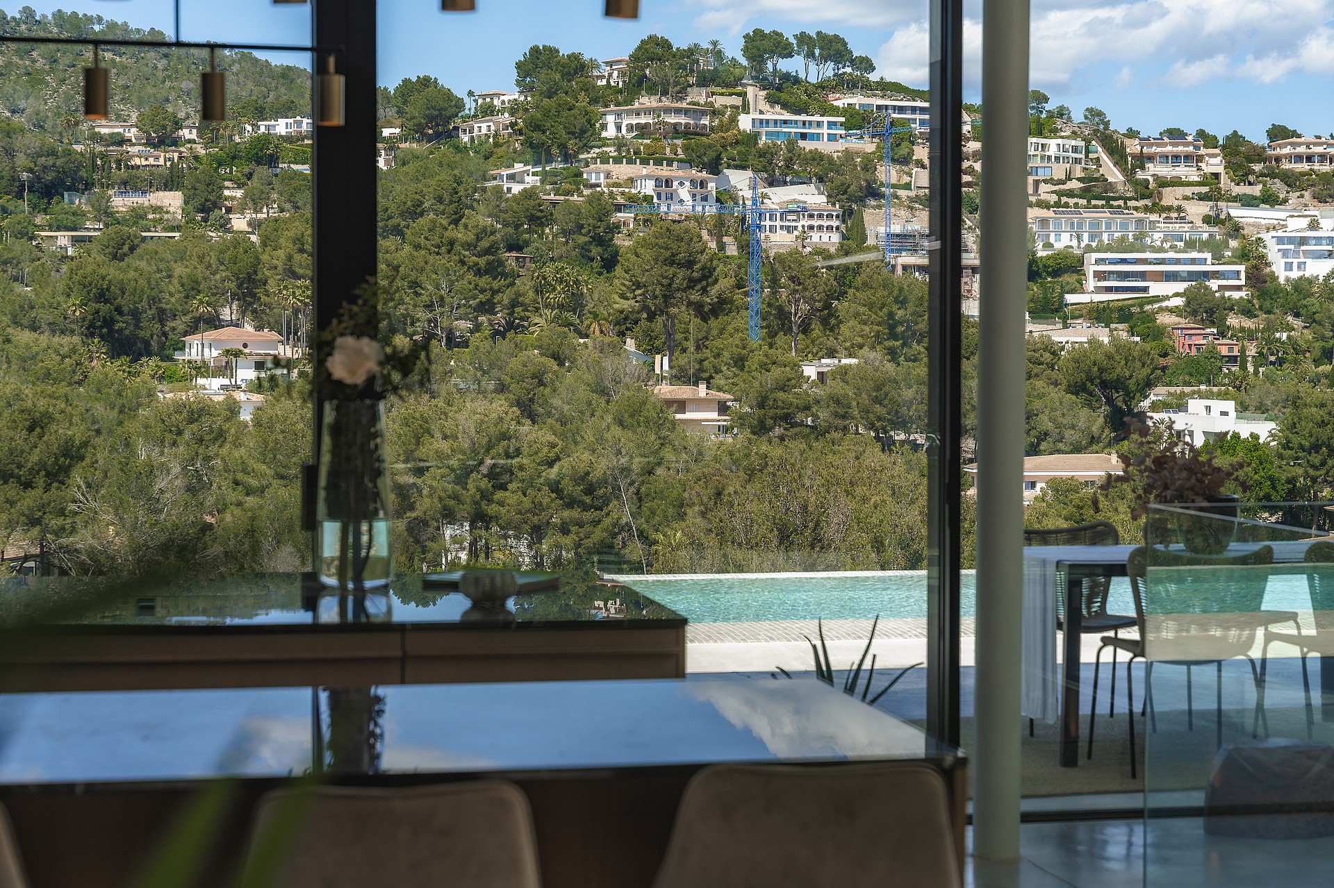 Interior view through floor-to-ceiling glass doors overlooking a terrace with a pool and the forested hills of Son Vida.