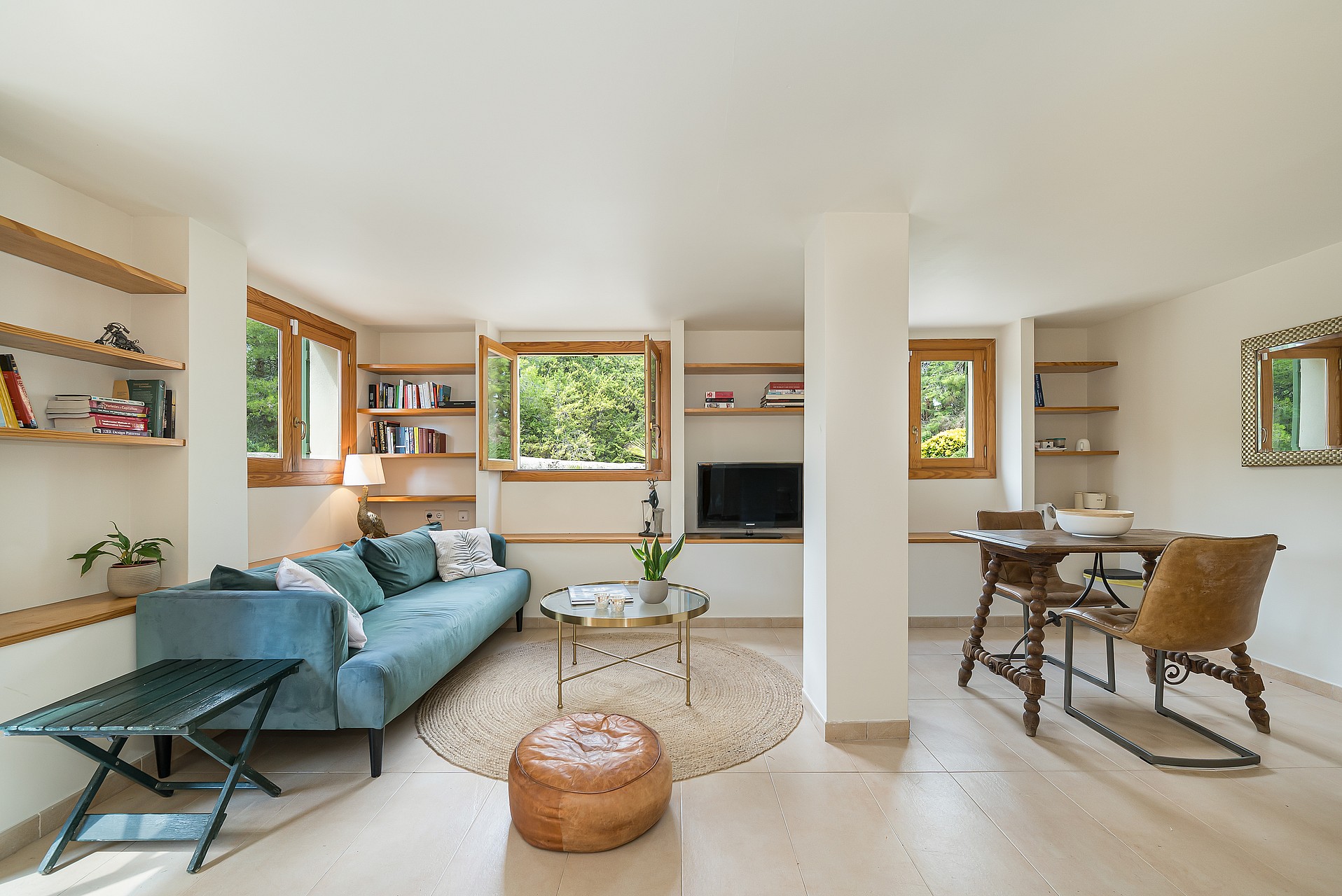 Bright living room featuring a blue velvet sofa, built-in wooden shelves, and casement windows showing garden greenery.