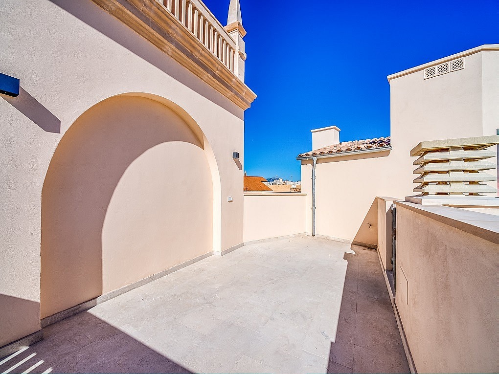 Empty rooftop terrace in Old Town with beige stucco walls, a large arched niche, and views toward traditional tiled rooftops.