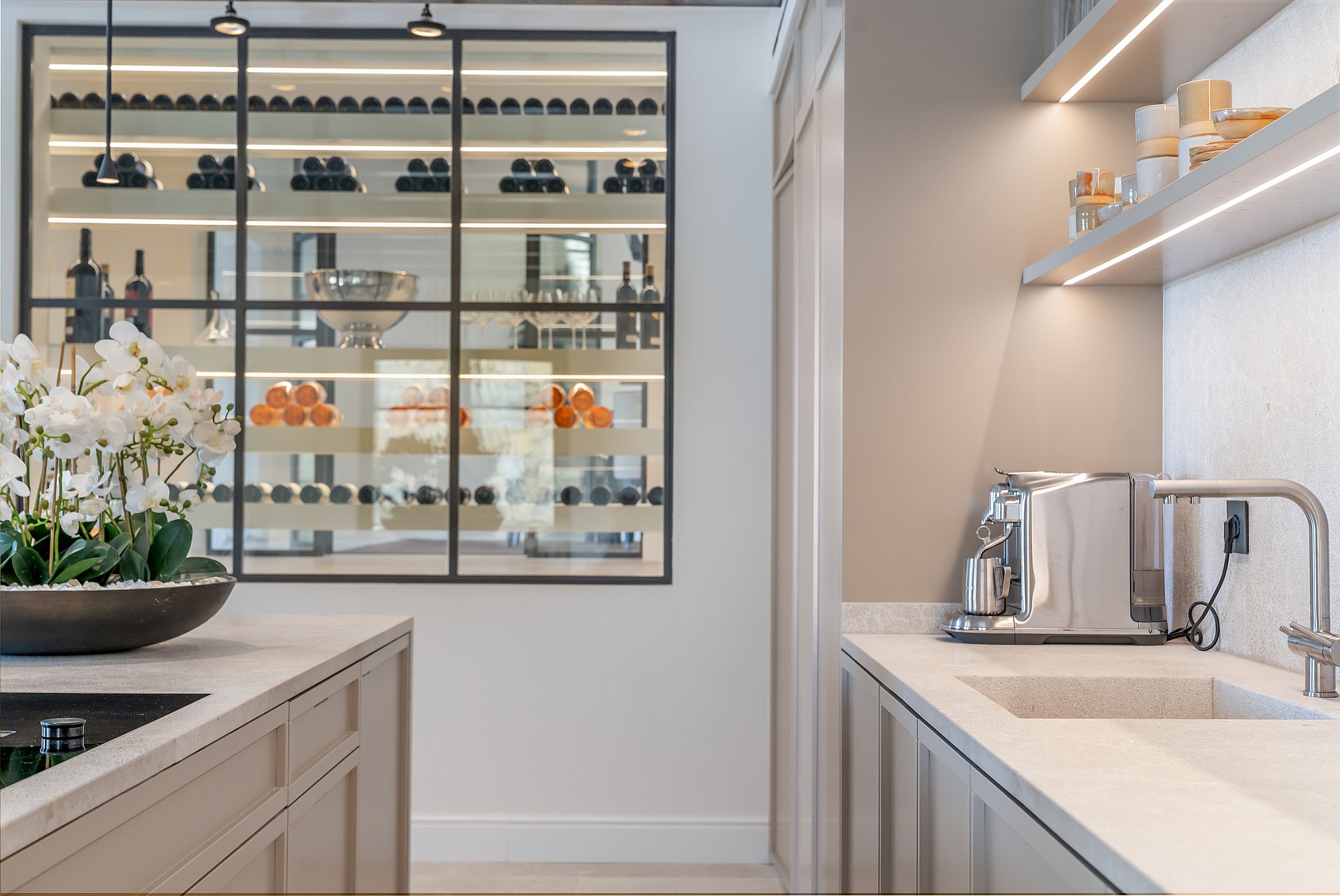 View from a kitchen island toward a temperature-controlled wine storage area with glass and black metal framing.