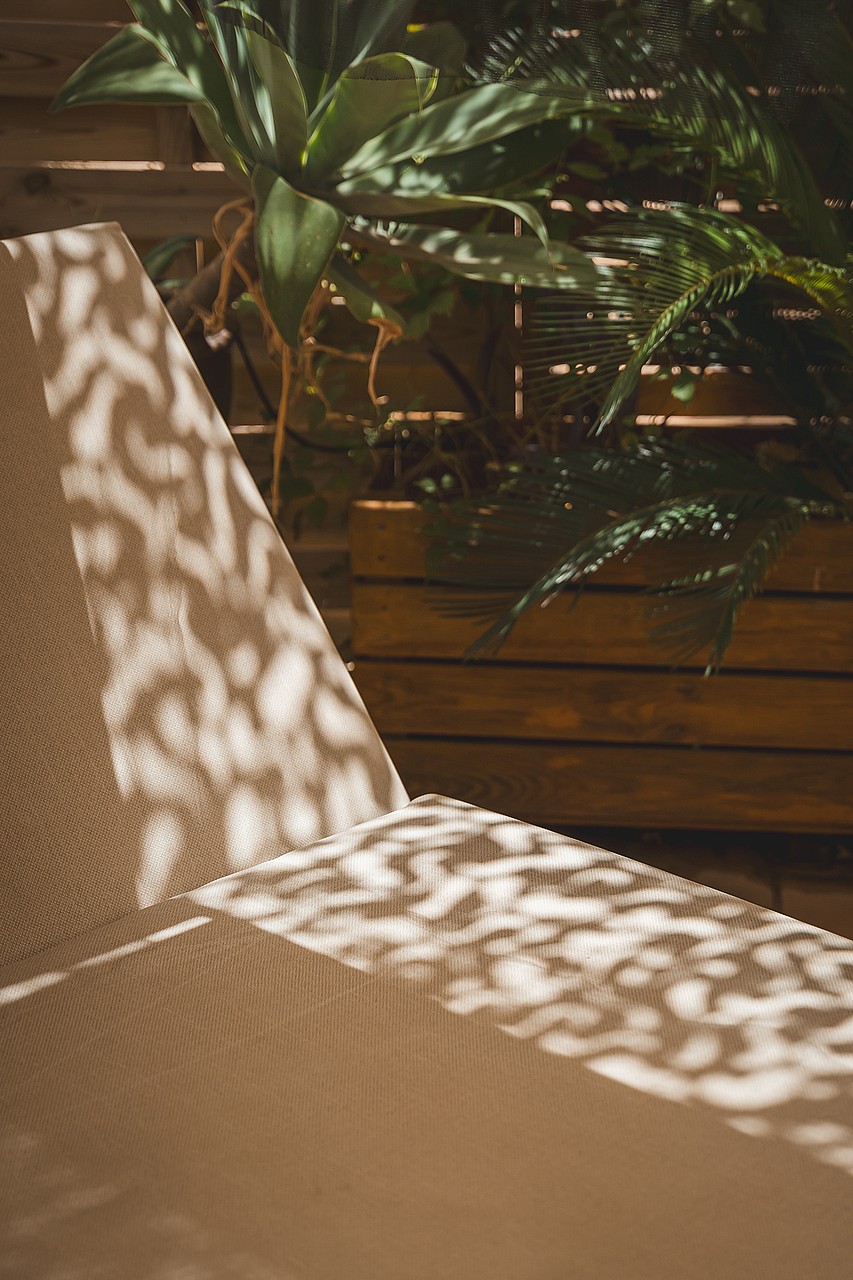 Close-up of a textured sun lounger on a terrace with wooden slats and tropical plants in the background.