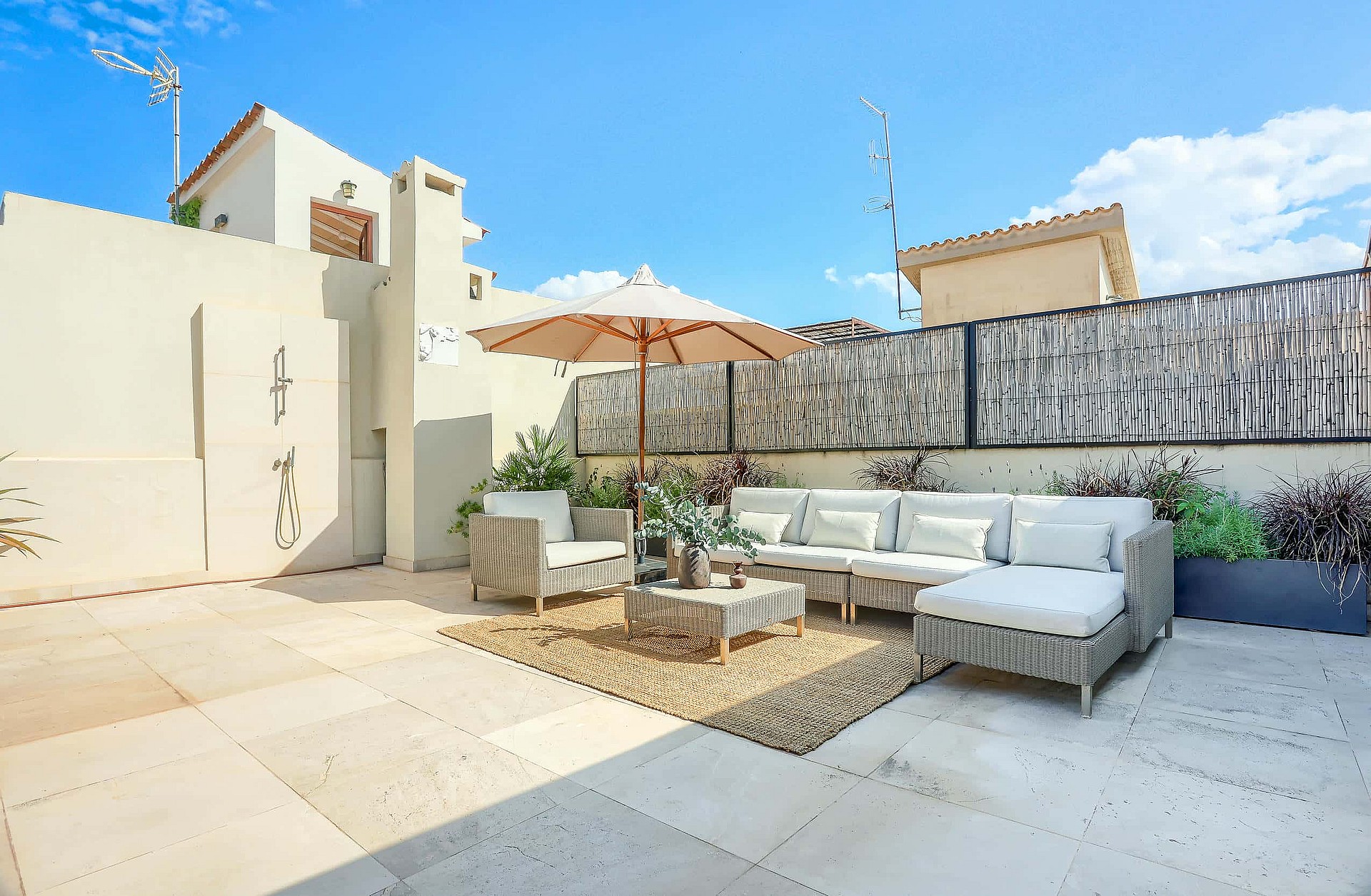 Rooftop terrace featuring light-colored stone paving, wicker-style outdoor sofa, and a central umbrella under a clear sky.