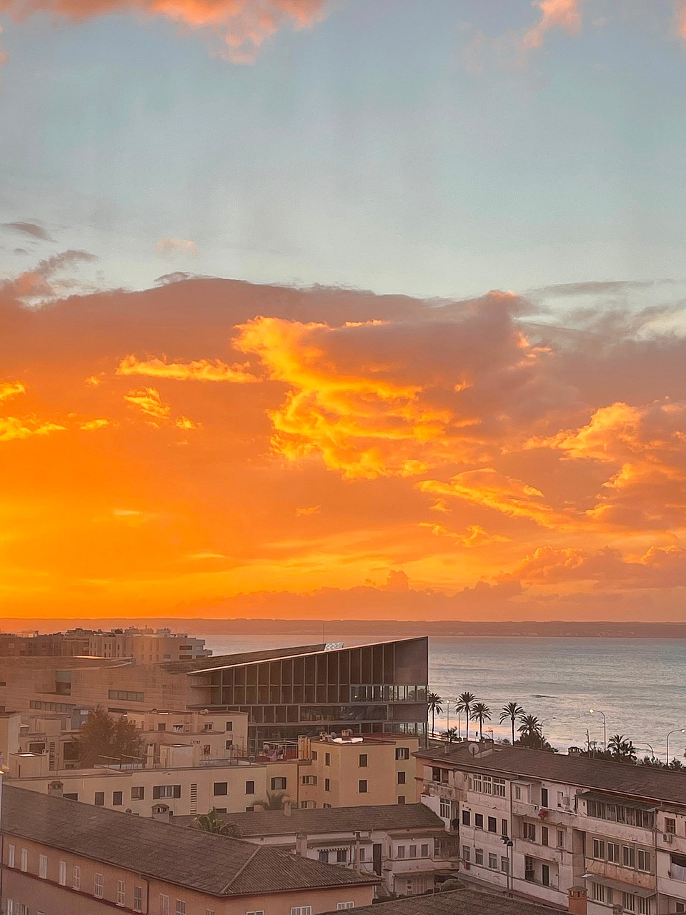 High-angle view overlooking old town rooftops and the sea during a vibrant orange and pink sunset.