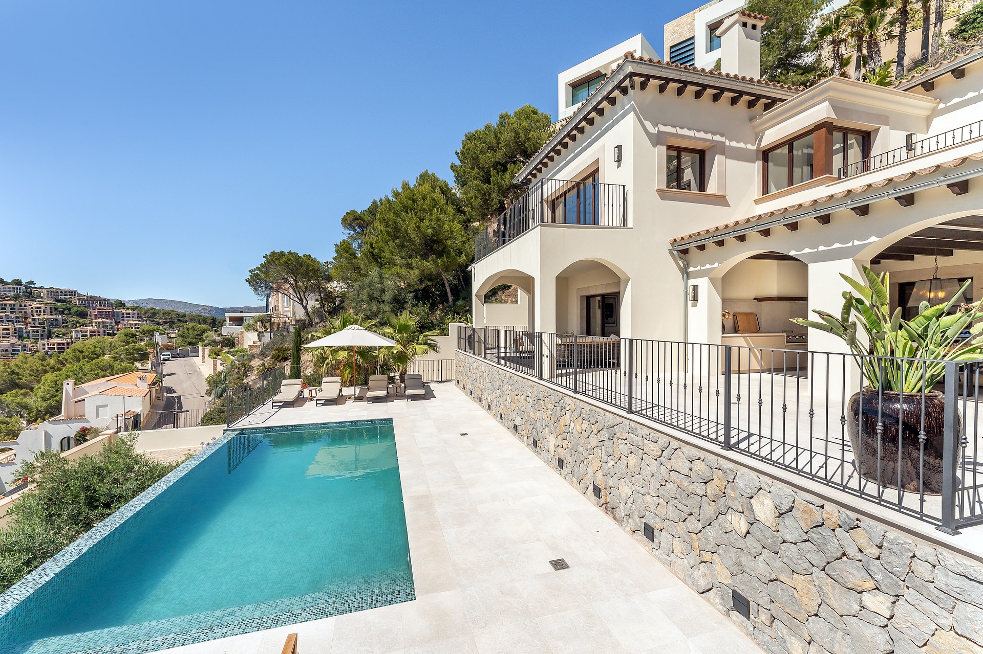 Exterior view of a cream stucco villa featuring arched terraces, wrought iron railings, stone walls, and a pool.