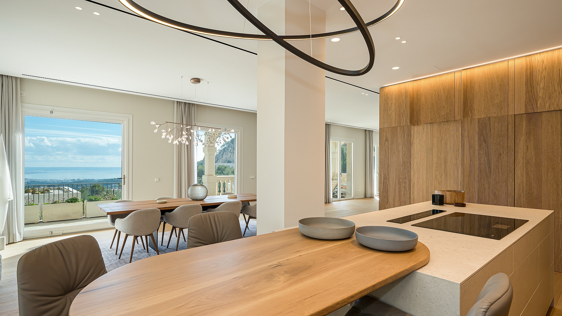 Open plan kitchen with light wood breakfast bar and modern dining set overlooking the Mediterranean coastline.
