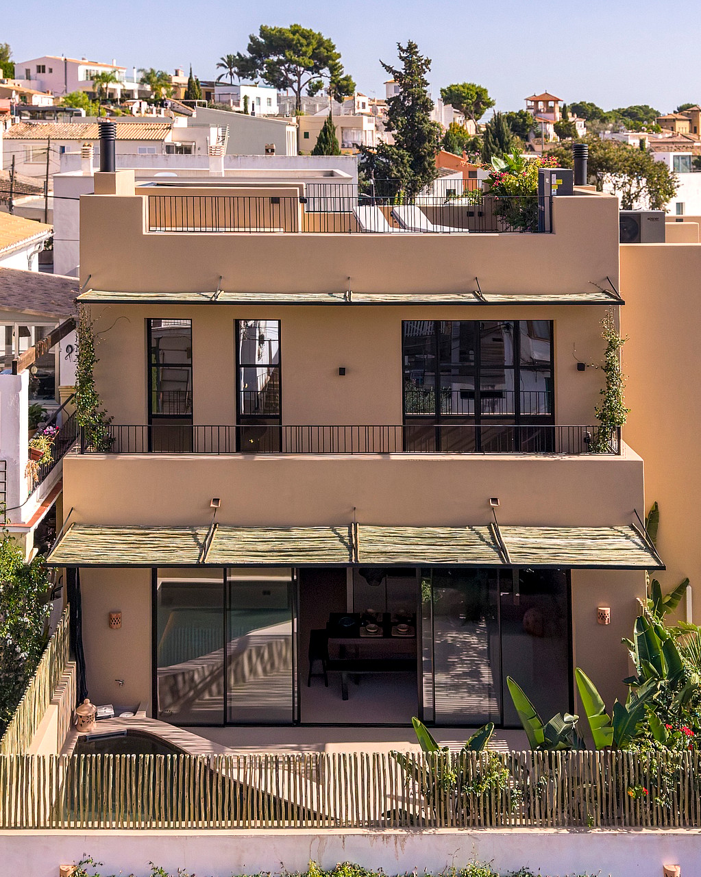 Front view of a two-story beige townhouse featuring modern black window frames, metal awnings, and glass sliding doors.