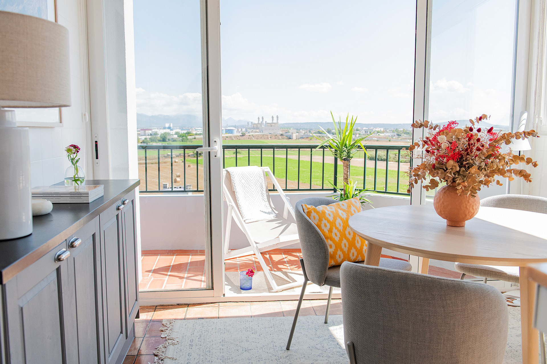 Dining room with a round wooden table, white chairs, and glass sliding doors opening to a balcony with mountain views.