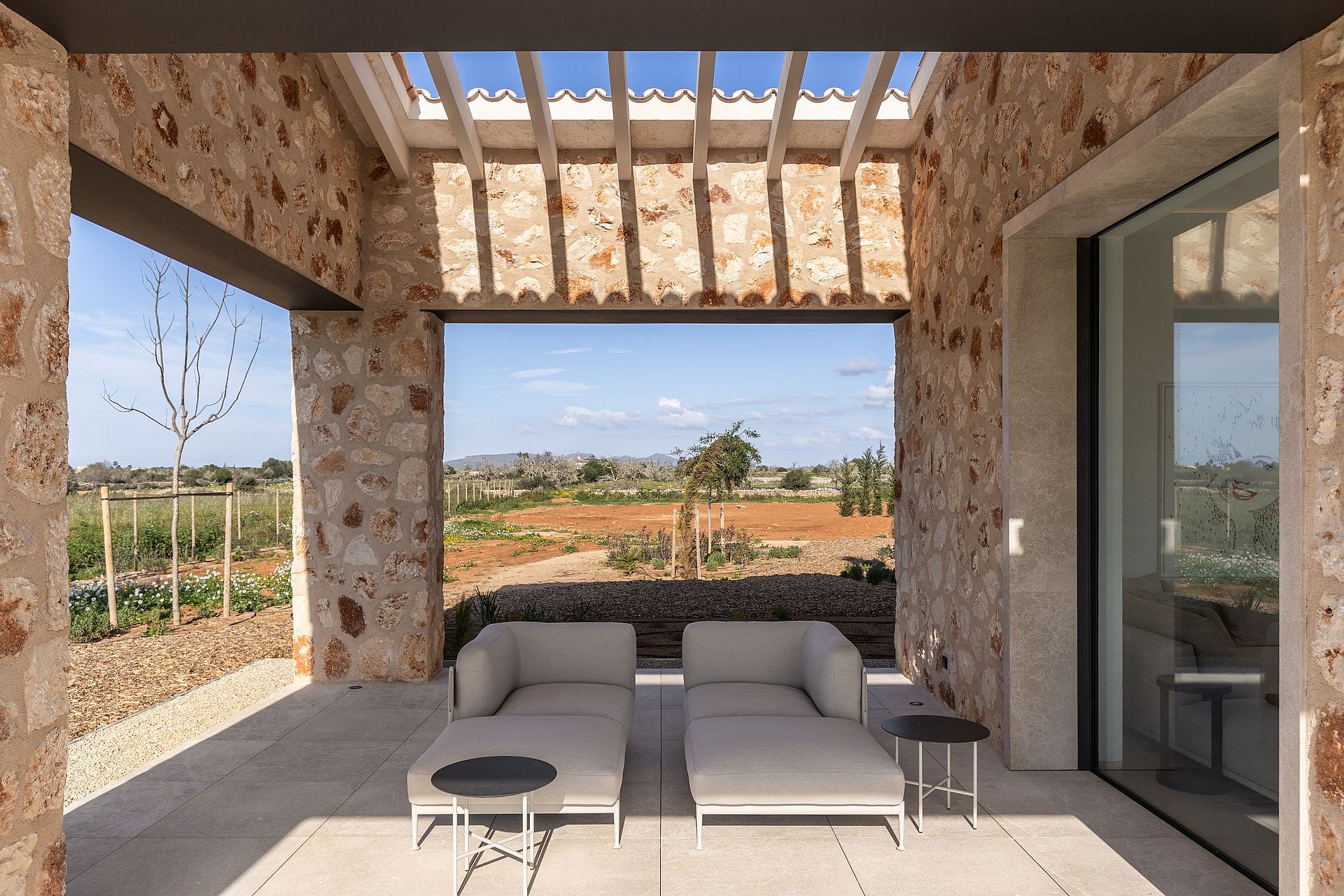 A stone-walled covered patio with modern outdoor seating, overlooking a rural landscape and distant mountains.