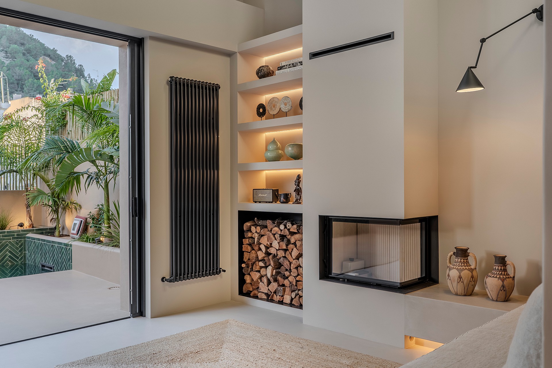 Modern living room featuring a glass-enclosed corner fireplace, built-in shelving, and sliding doors opening to a pool terrace.