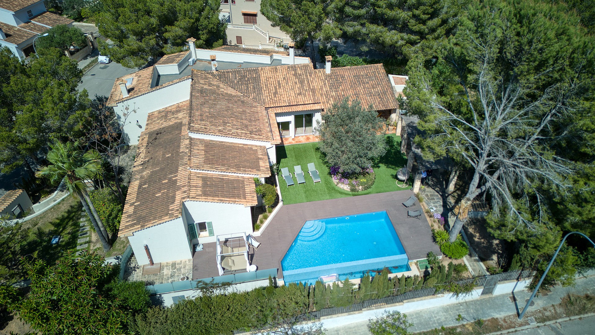 High-angle aerial shot of a residential villa featuring a terracotta tile roof, a swimming pool, and landscaped garden area.