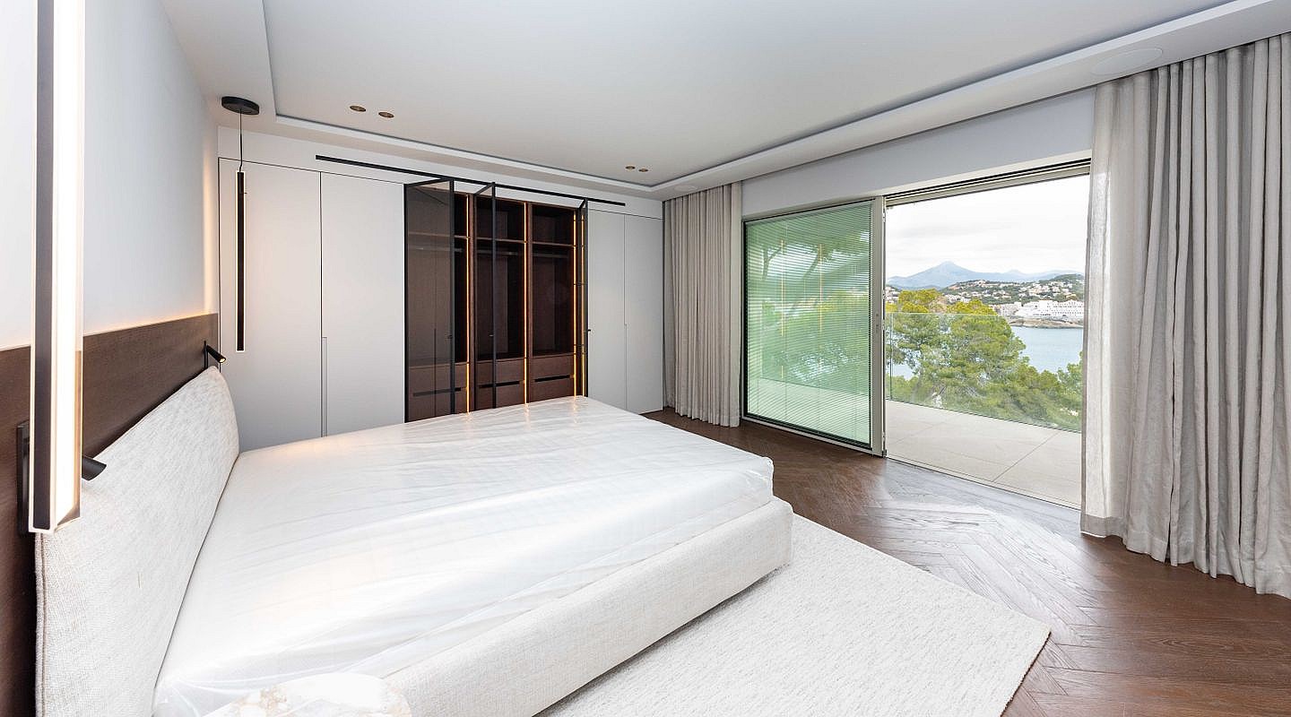 A modern bedroom featuring a large bed with an upholstered headboard, adjacent to a walk-in closet with dark glass doors.