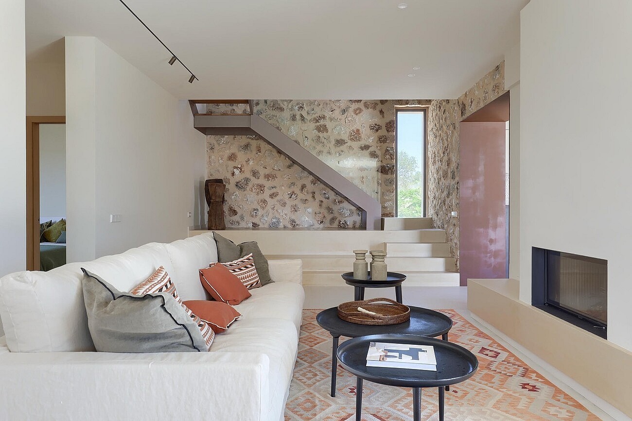 Interior view of a living room featuring a cream sofa, stone accent wall, inset fireplace, and floating staircase steps.