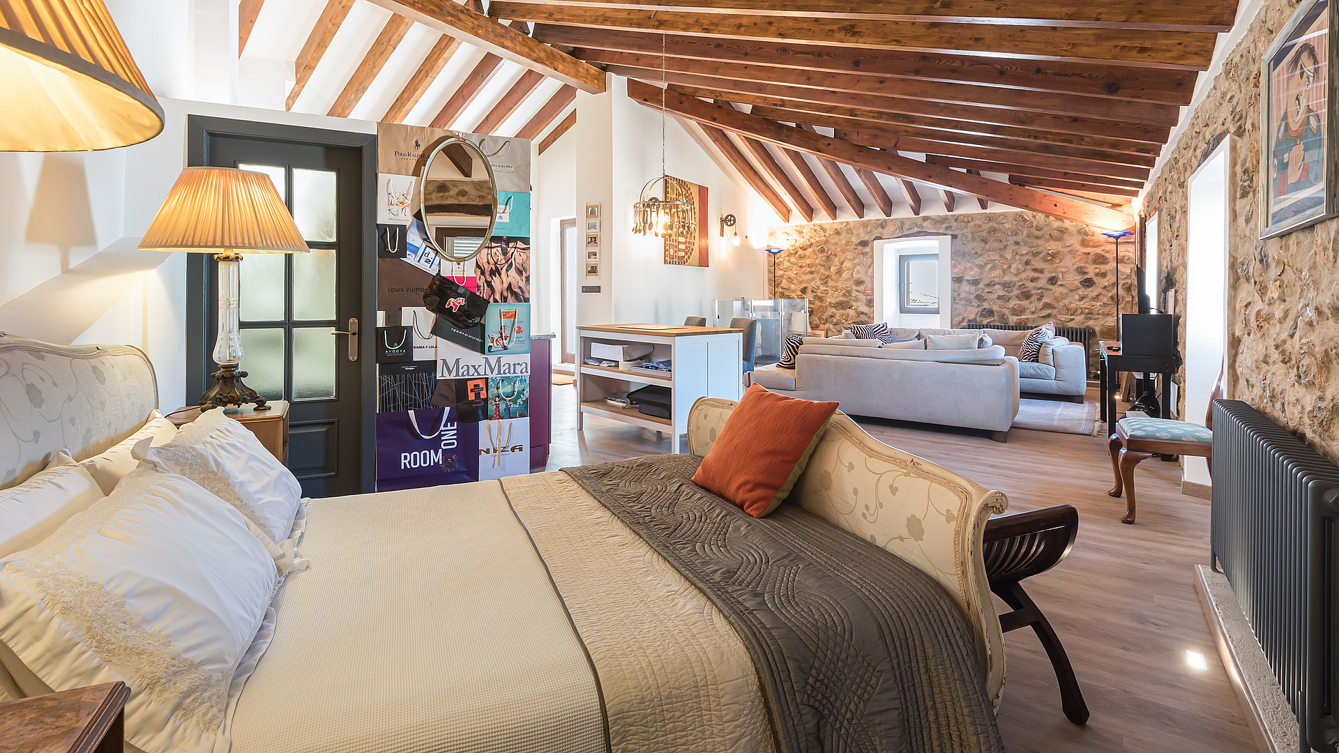 Loft-style bedroom featuring exposed wooden beams, stone walls, and an integrated living space.