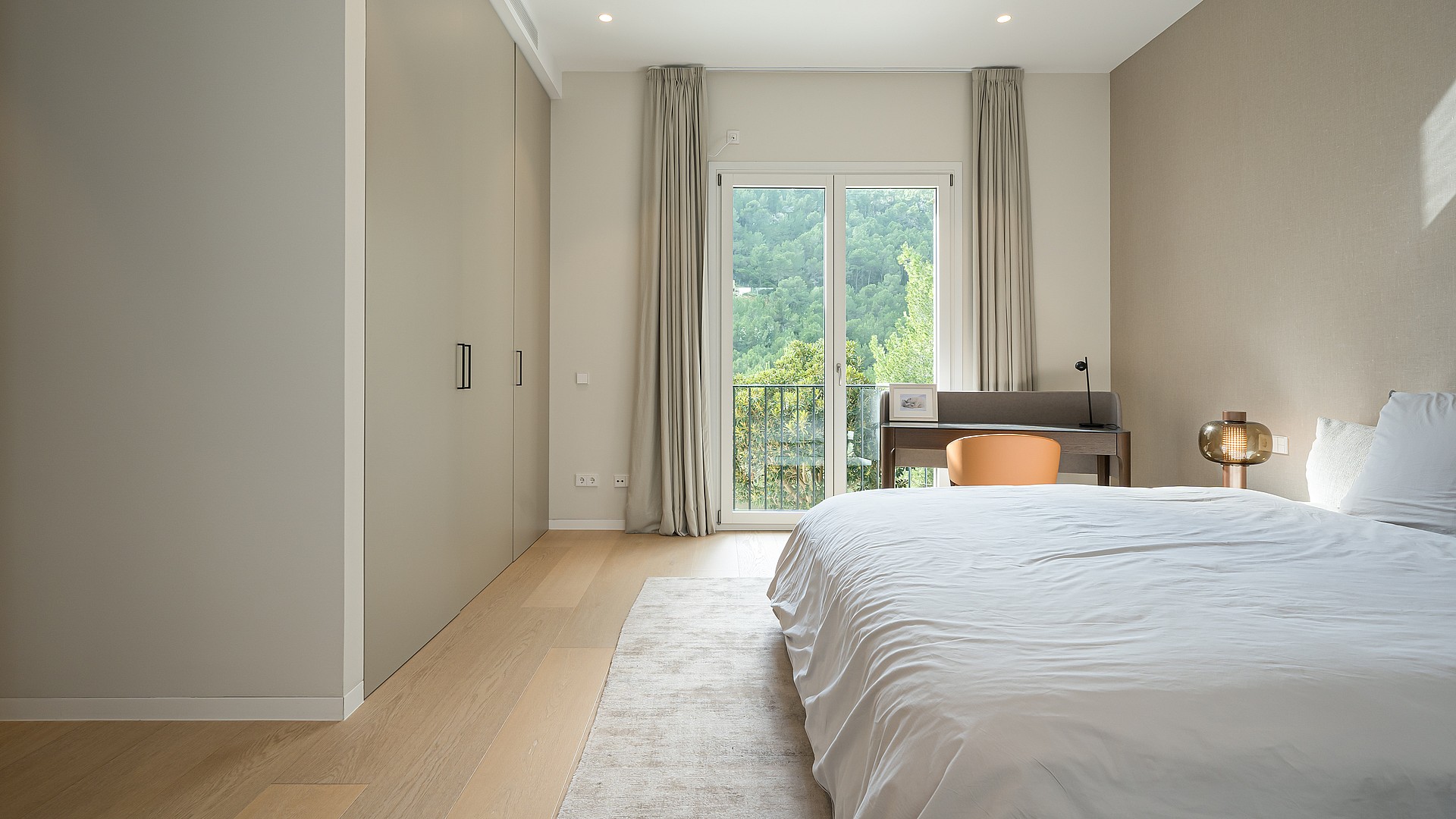 Bedroom with light wood floors, built-in wardrobes, a desk near the balcony door, and white bedding in a Son Vida villa.