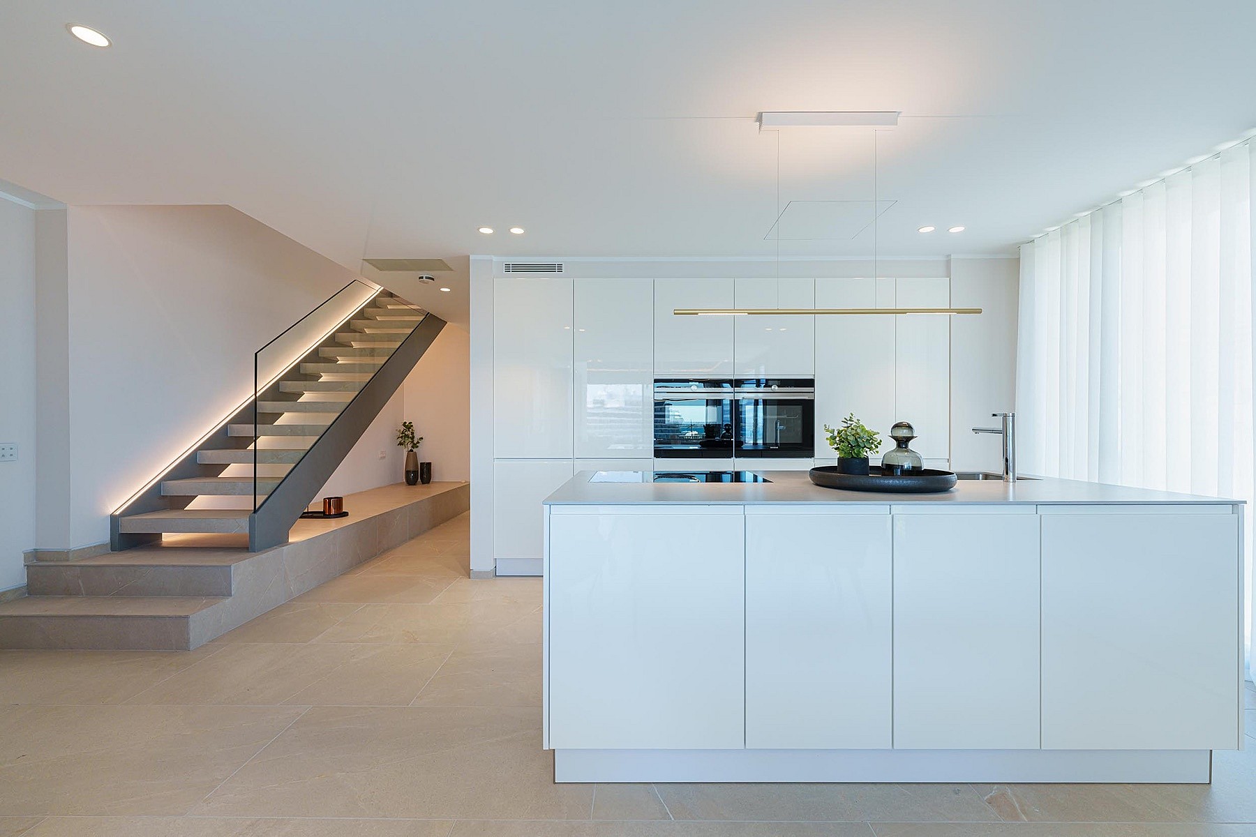 Cocina blanca moderna con isla y escalera abierta con iluminación LED integrada en un piso luminoso.