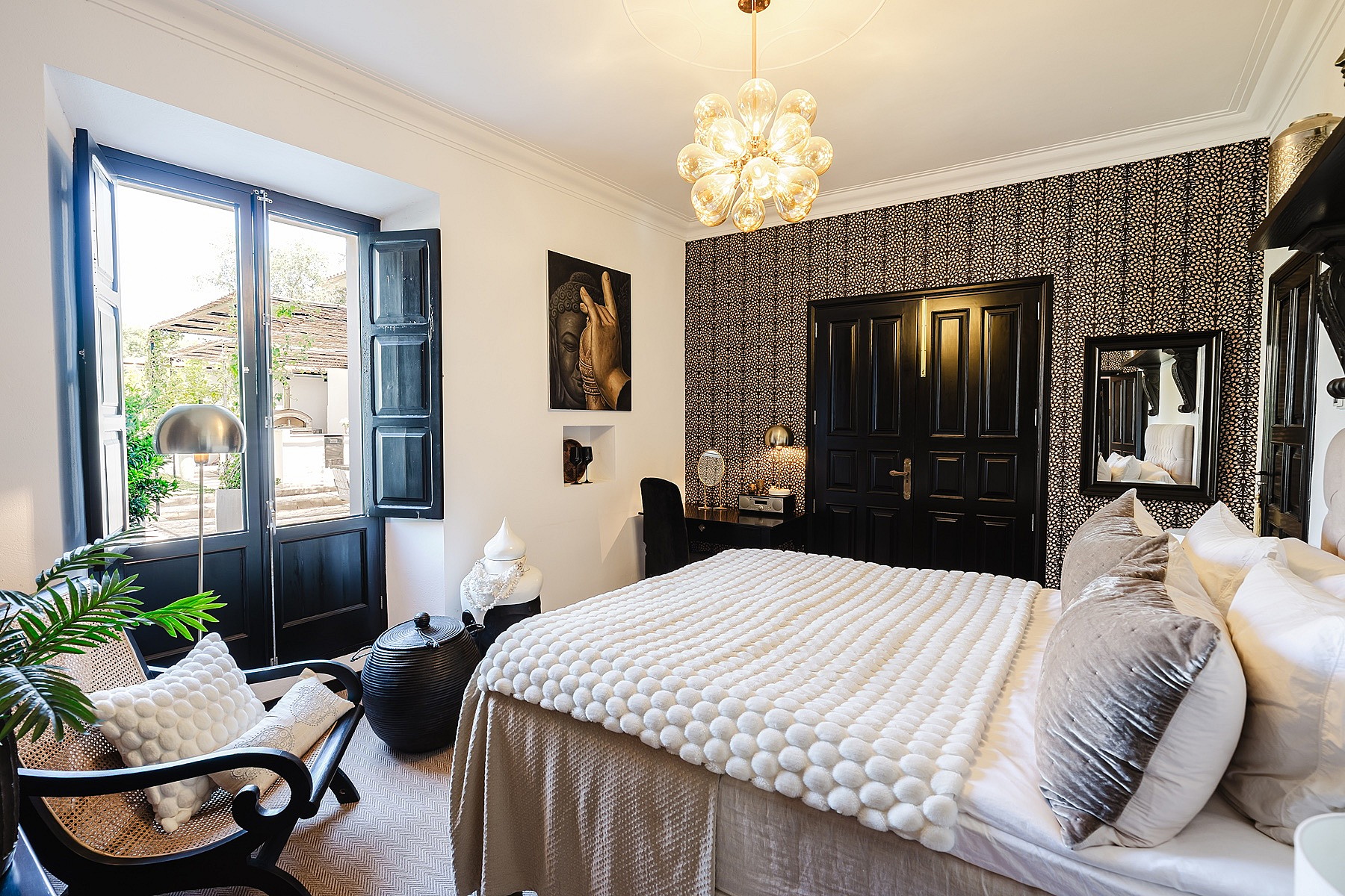 A bedroom with white walls, a black and white patterned feature wall, and tall black French doors opening to a garden.
