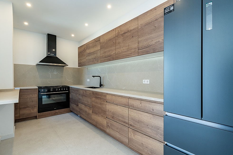 A modern kitchen in a townhouse featuring wood grain cabinets, dark appliances, stone countertops, and recessed ceiling lights.
