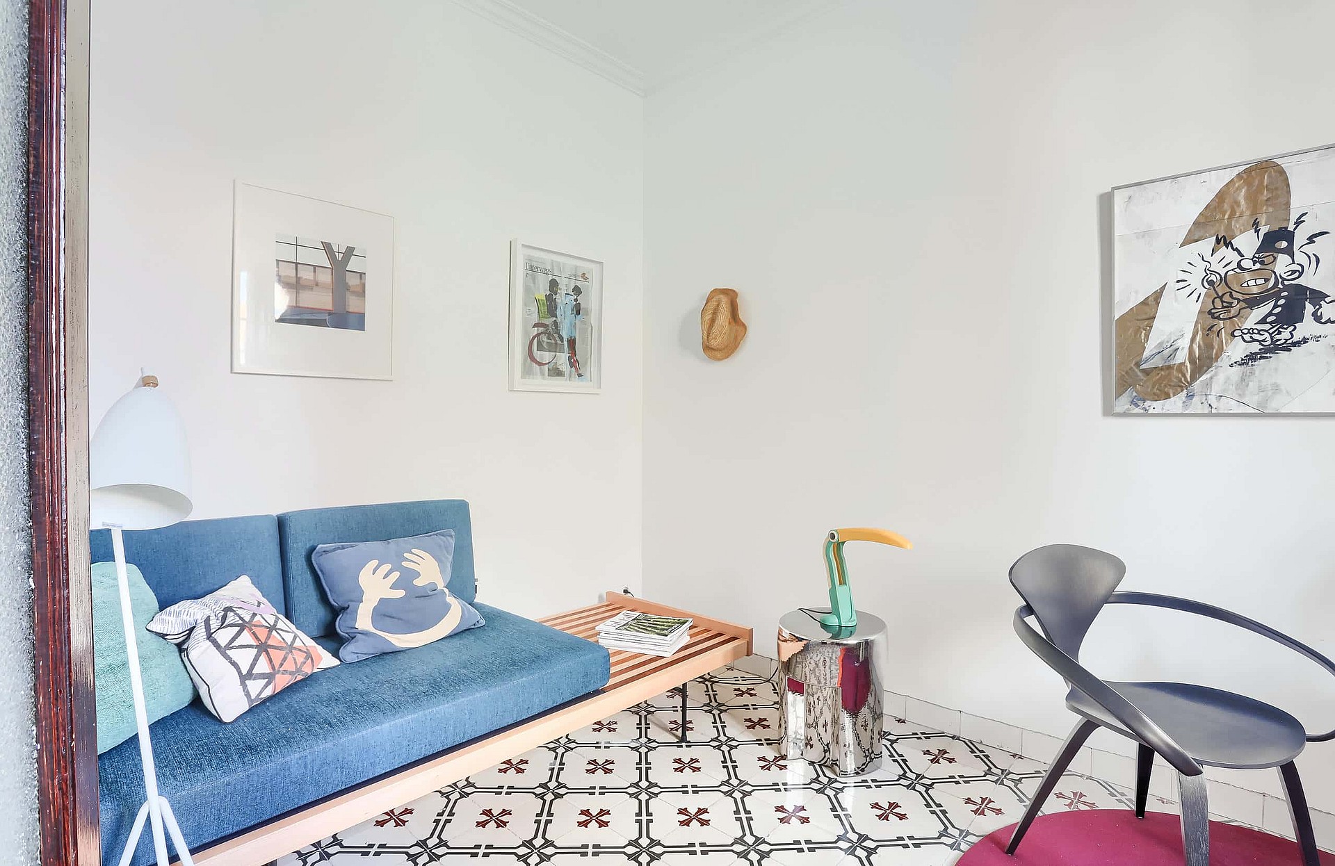 A small living space featuring a blue upholstered daybed, patterned floor tiles, a chrome side table, and a modern chair.