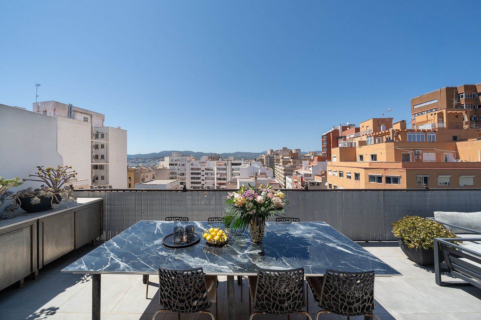 Outdoor dining table with marble top on a rooftop terrace overlooking Old Town buildings under a clear blue sky.