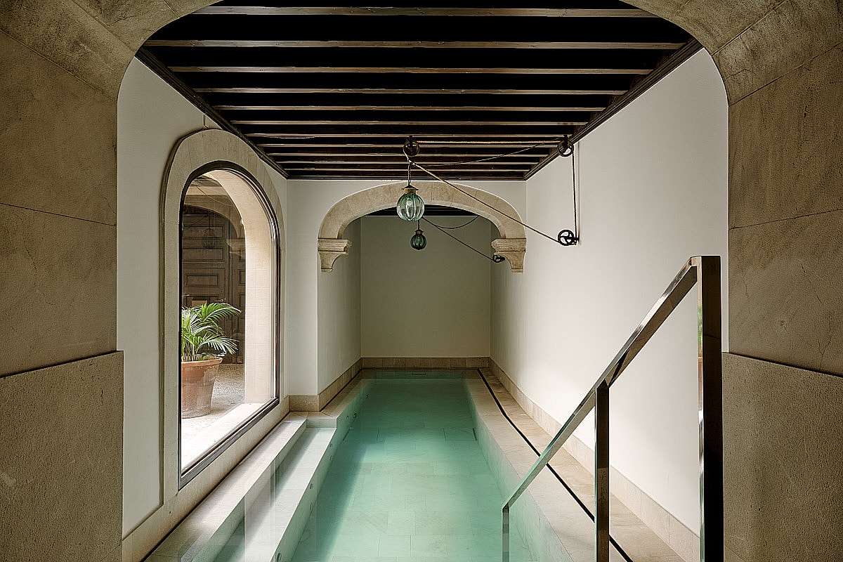 Indoor swimming pool featuring turquoise water, arched stone vault ceiling detail, minimalist contemporary design, and soft natural light