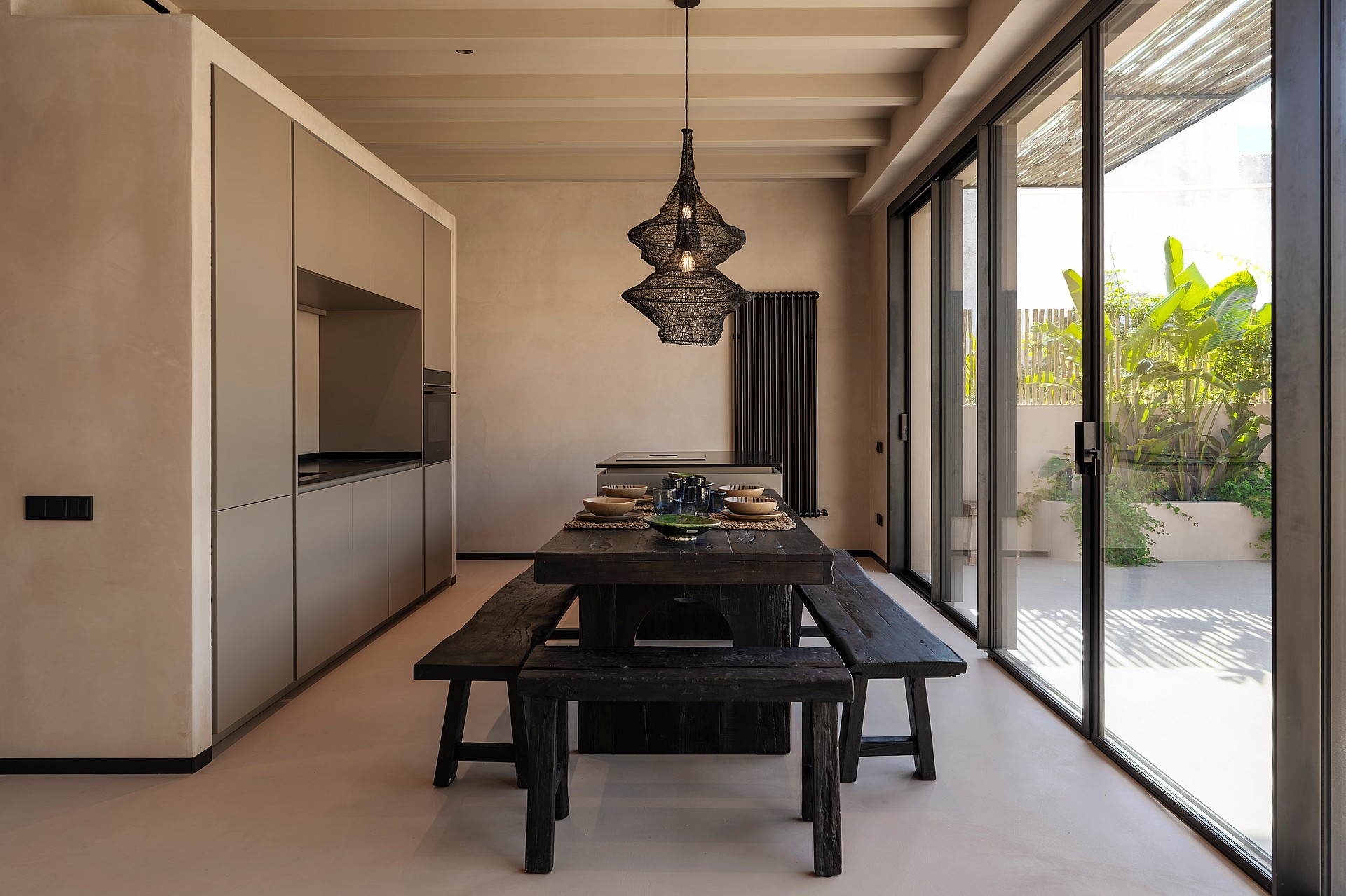 Modern kitchen with minimalist grey cabinetry and a dark wood dining table, opening onto a sunlit outdoor terrace.