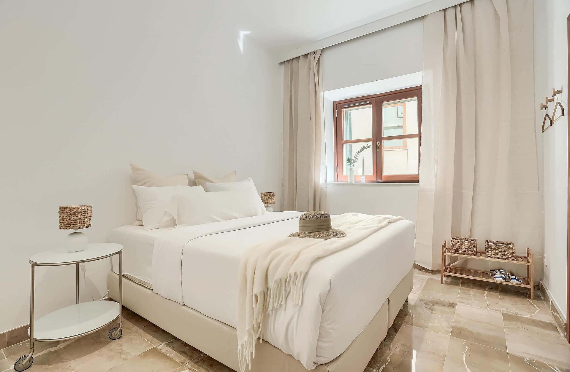 A bright bedroom with a queen-sized bed, white linens, beige curtains, and polished marble flooring in an Old Town townhouse.