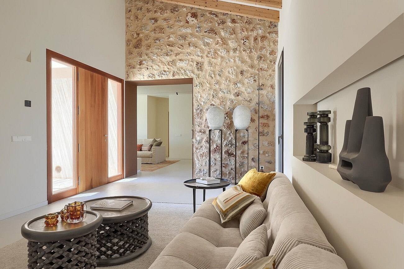 Interior view of a living area featuring a tall exposed stone feature wall, vaulted ceilings, and a light-colored sofa.