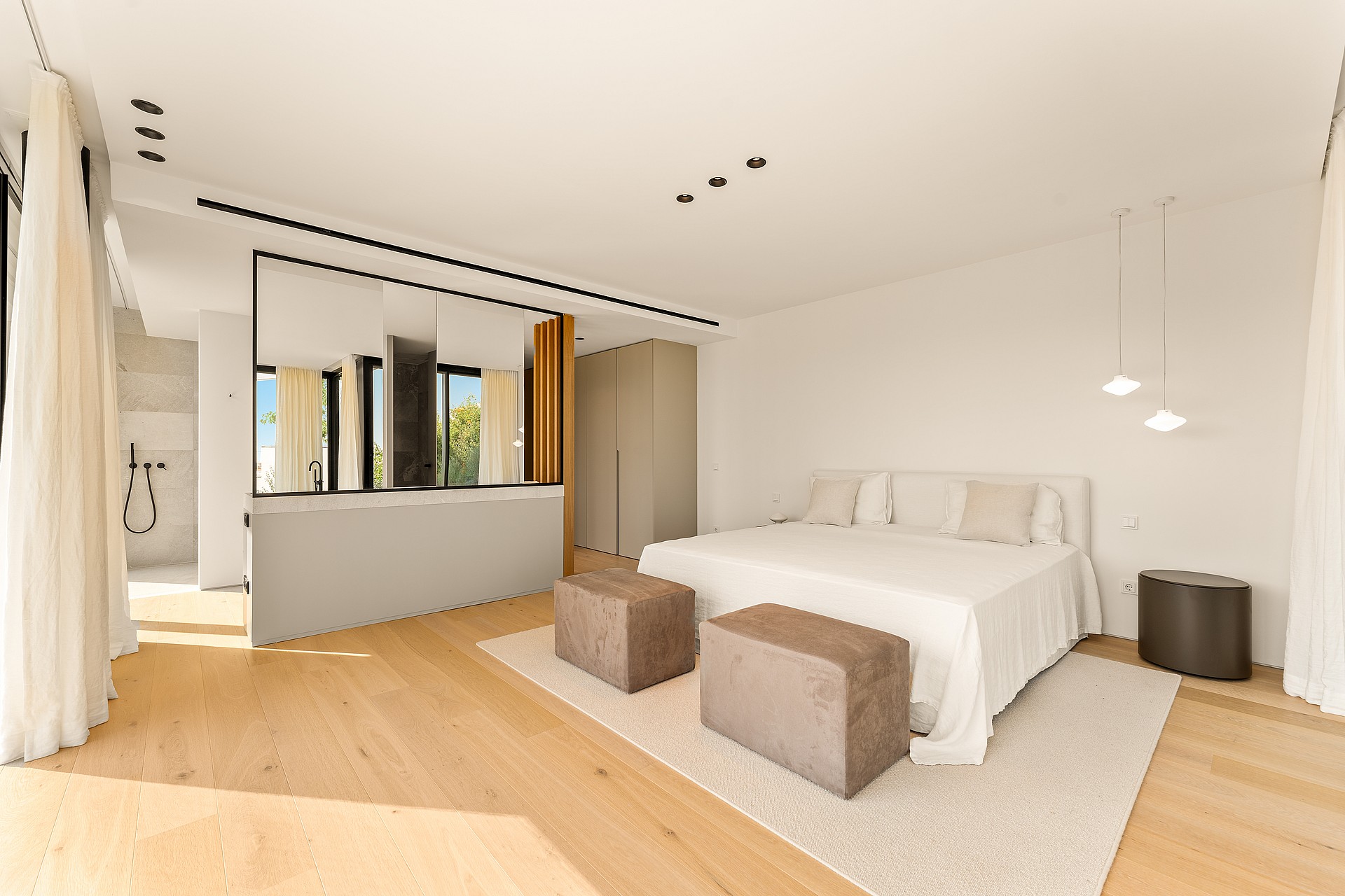 Contemporary bedroom with light oak flooring, white walls, and a central partition wall with a mirror and glass window.