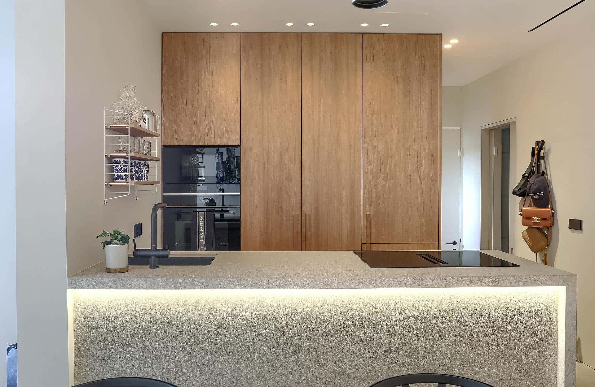 Modern kitchen with full-height oak cabinetry, a light stone kitchen island with integrated LED lighting, and built-in oven.