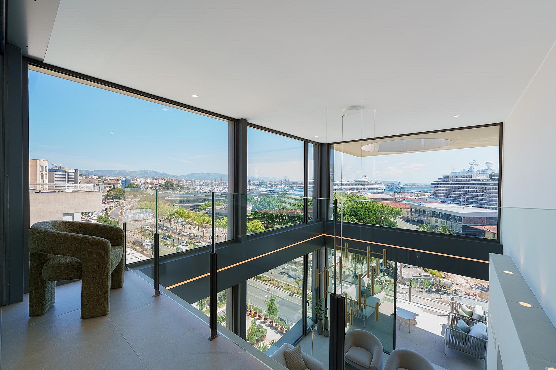 Salón de doble altura con paredes de cristal, una butaca de terciopelo y vistas al puerto.