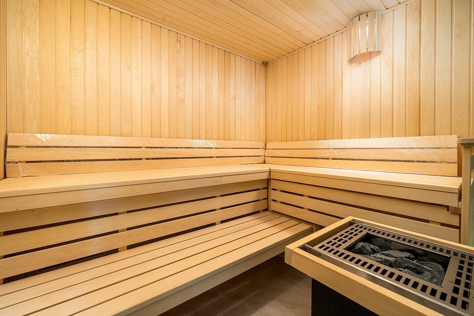A modern home sauna featuring natural light wood wall cladding and tiered wooden bench seating, with a central electric heater.